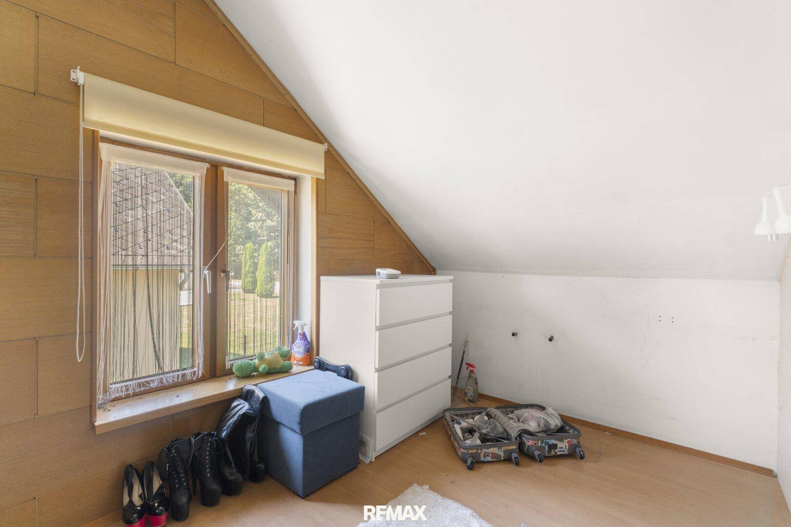 Dachgeschosszimmer mit schräger Decke, Holzboden und einem Fenster, das Tageslicht hereinlässt.