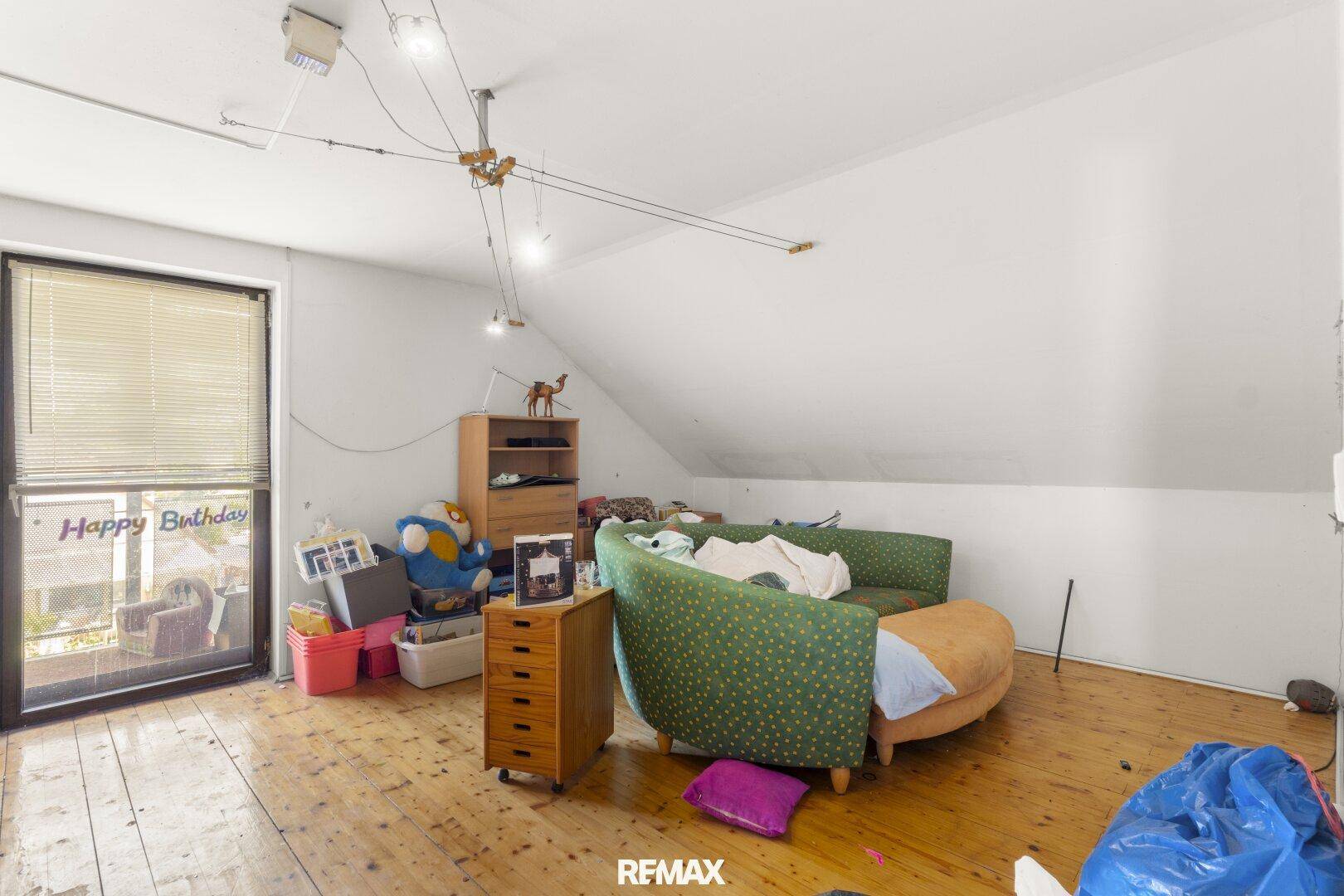 Dachgeschosszimmer mit schräger Decke, Holzdielenboden und Zugang zu einem kleinen Balkon.