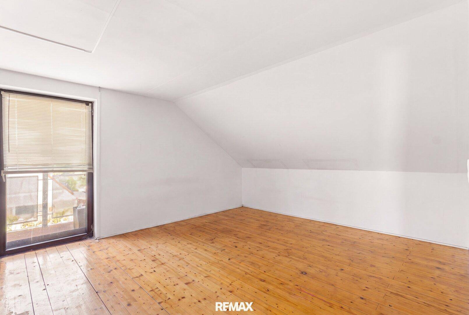Geräumiges Dachgeschosszimmer mit Holzdielenboden und direktem Zugang zu einem Außenbereich.