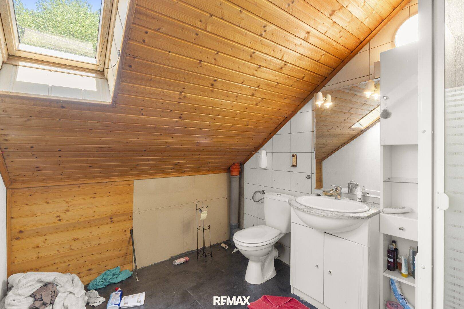Dachgeschoss-Badezimmer mit Holzdecke, Dachfenster, WC und Waschbecken, bietet viel Tageslicht.