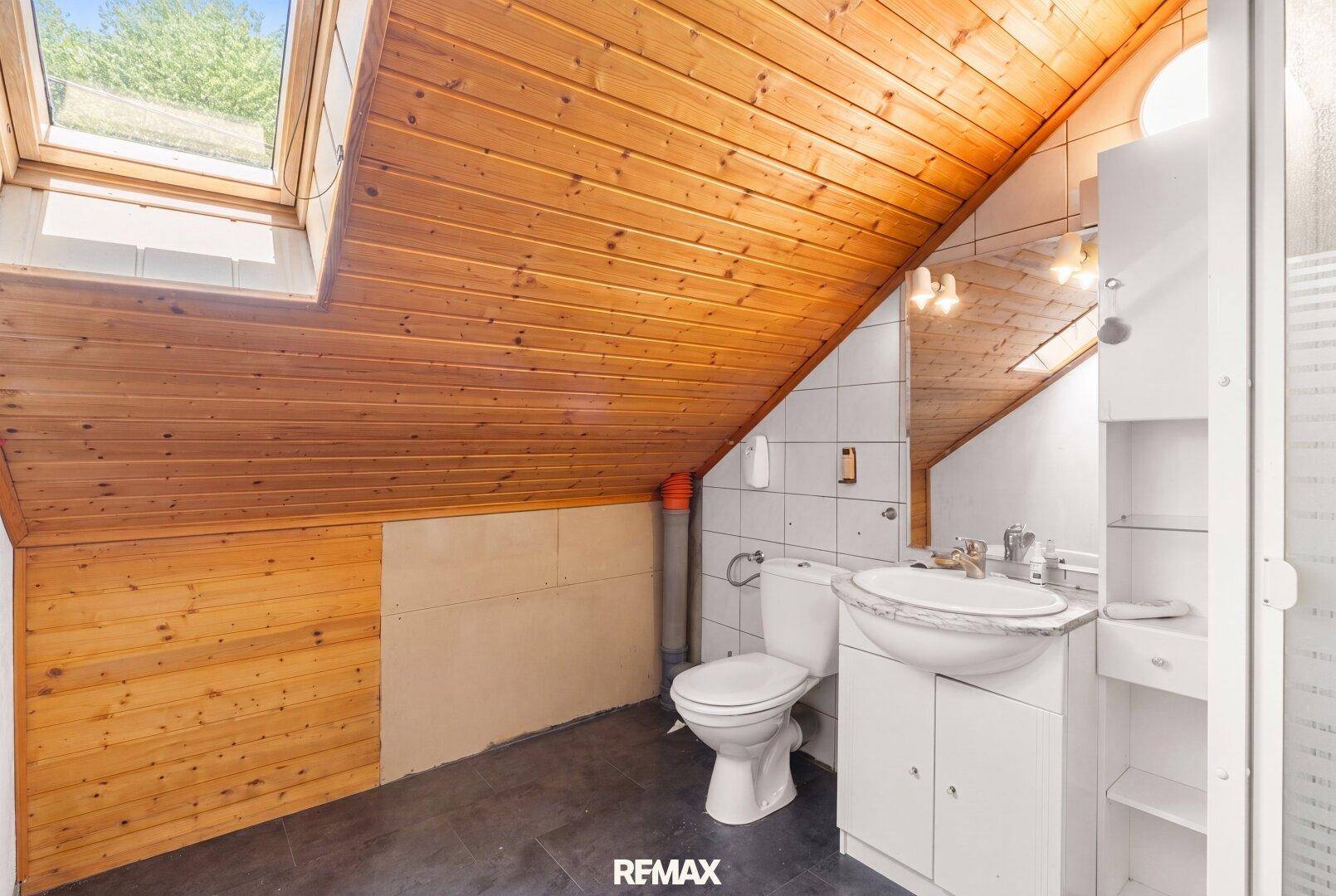 Helles Dachgeschoss-Badezimmer mit Holzdecke, Dachfenster und grundlegender Ausstattung.