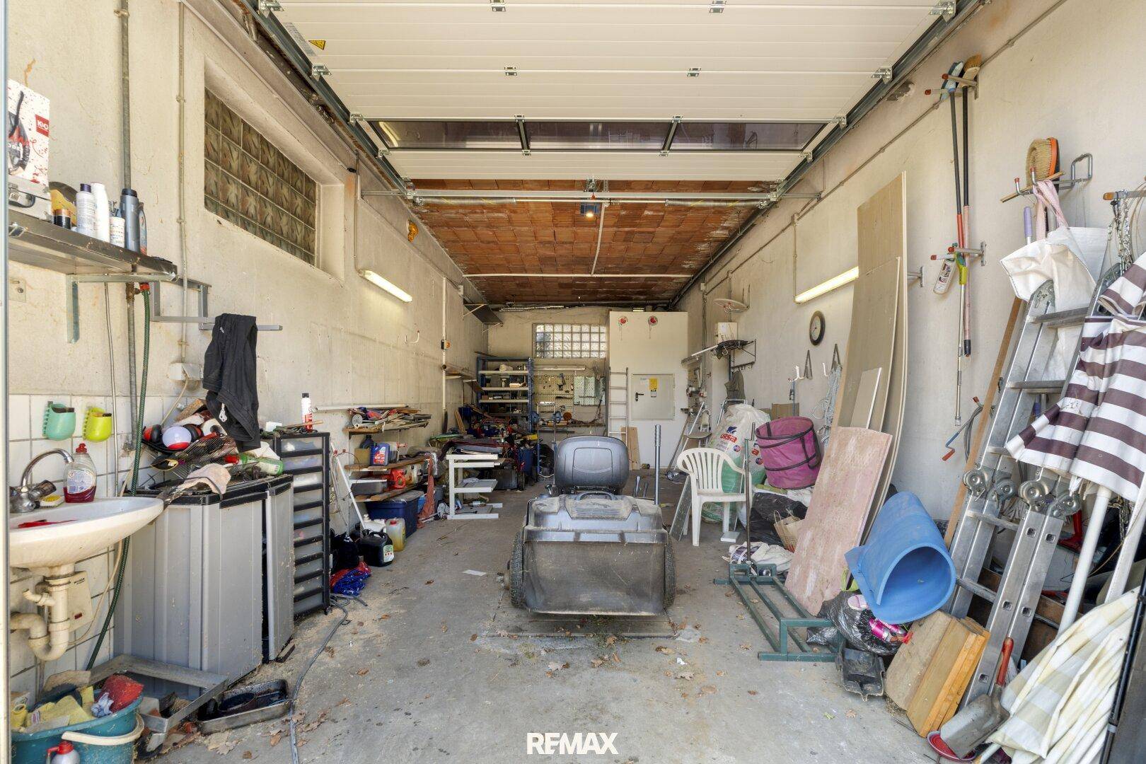 Geräumige Garage mit Rolltor, Waschbecken und viel Stauraum, ideal als Werkstatt oder Abstellfläche.
