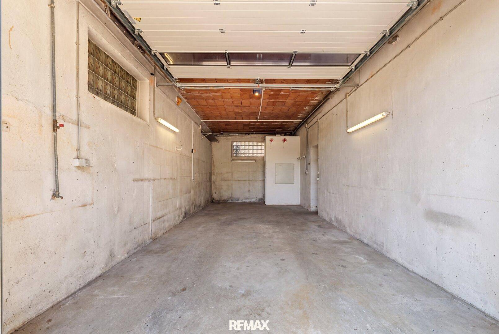 Leere Garage mit Rolltor, Betonwänden und Holzdecke, bereit für Fahrzeuge oder Lagerung.