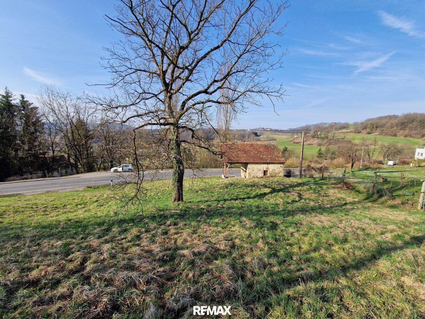 Weitläufige Landschaft mit historischem Gebäude, alter Eiche und Blick auf die umliegenden Hügel.