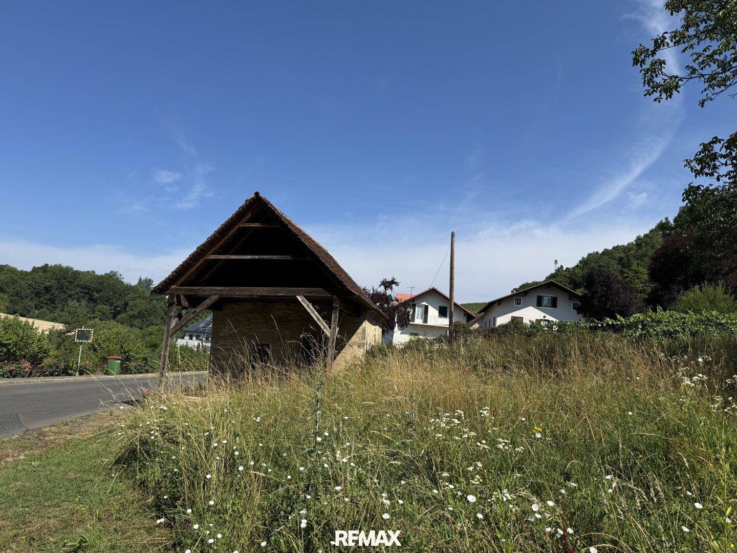 Rustikales Steingebäude mit offenem Holzdachstuhl und Blick auf weitere Häuser in der Ferne.