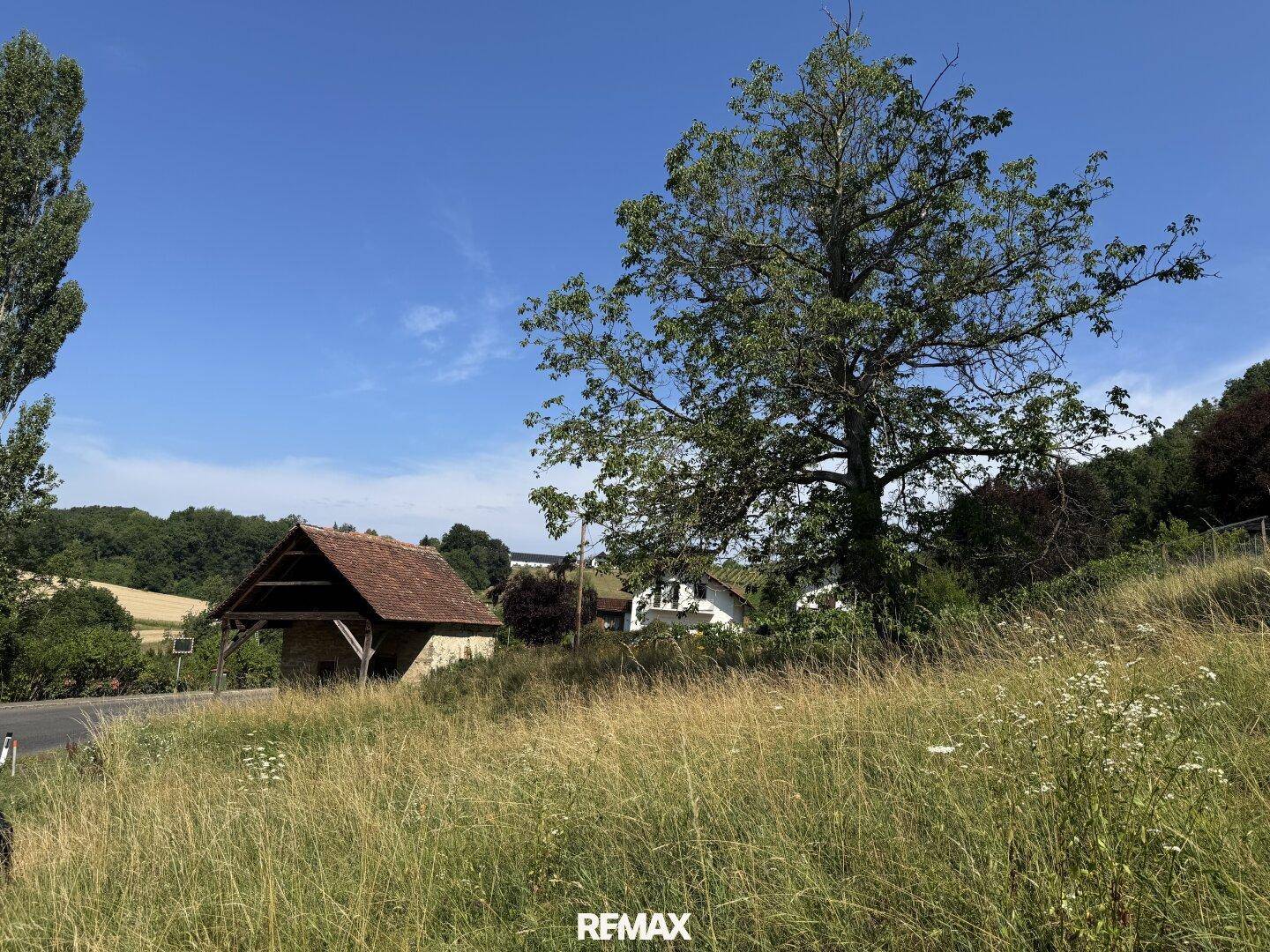 Panoramablick auf ein altes Steingebäude, umgeben von Natur und weiteren Häusern in der Ferne.