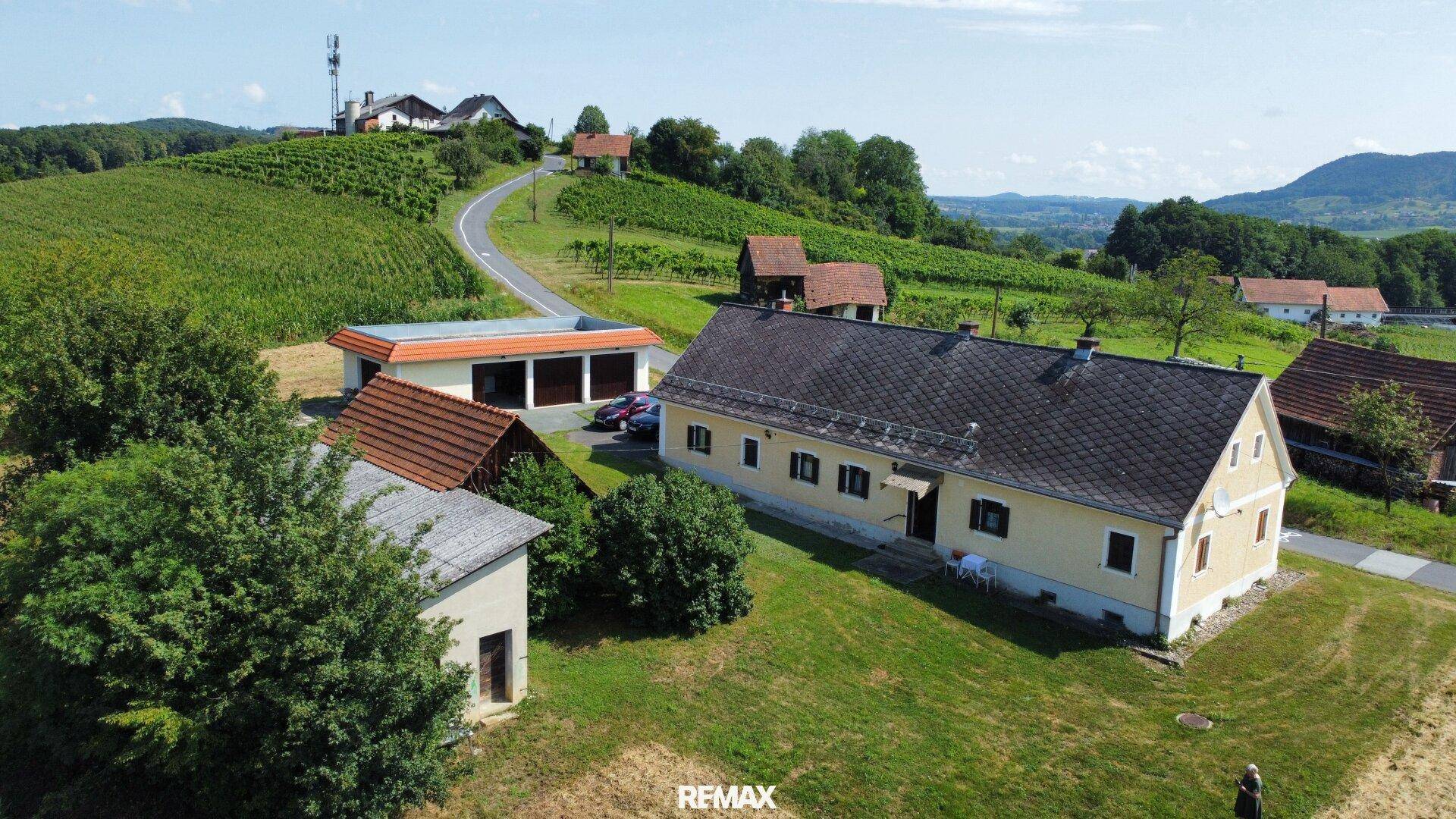 Luftaufnahme eines ländlichen Anwesens mit Hauptgebäude und Nebengebäuden, umgeben von Weinbergen und Feldern.