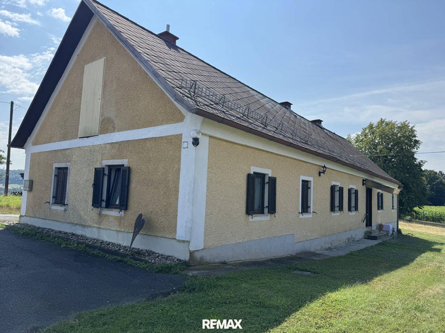 Seitenansicht eines traditionellen Landhauses mit gelber Fassade, dunklen Fensterläden und Satteldach.