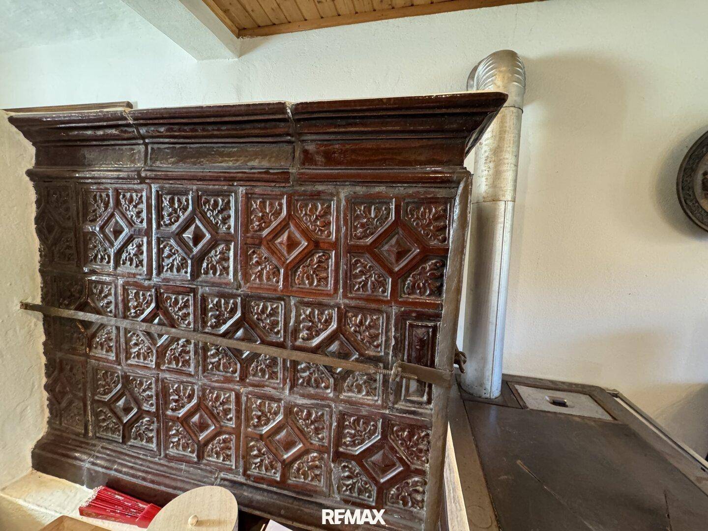 Detailaufnahme eines traditionellen, reich verzierten Kachelofens mit dunklen Fliesen und Metallrohr.