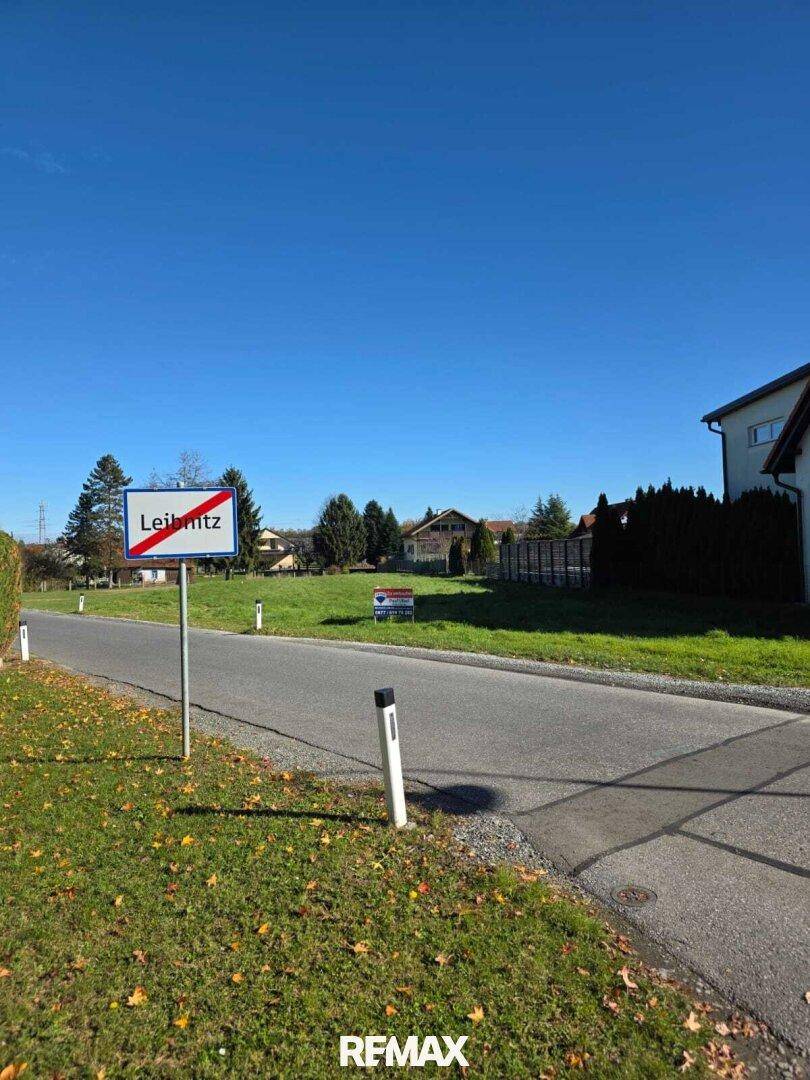 Sonniger Blick auf die Ortseinfahrt von Leibnitz mit Straßenschild und umliegender Landschaft.