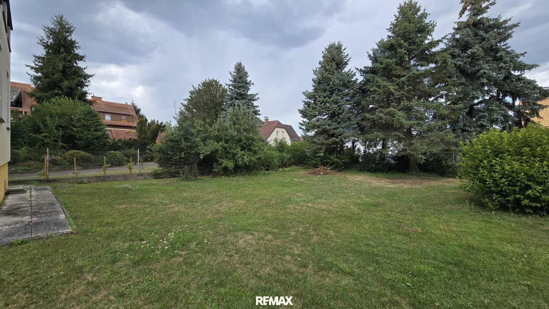 Weitläufiger Gartenbereich mit Rasenfläche und hohen Bäumen im Hintergrund, bietet viel Grün.