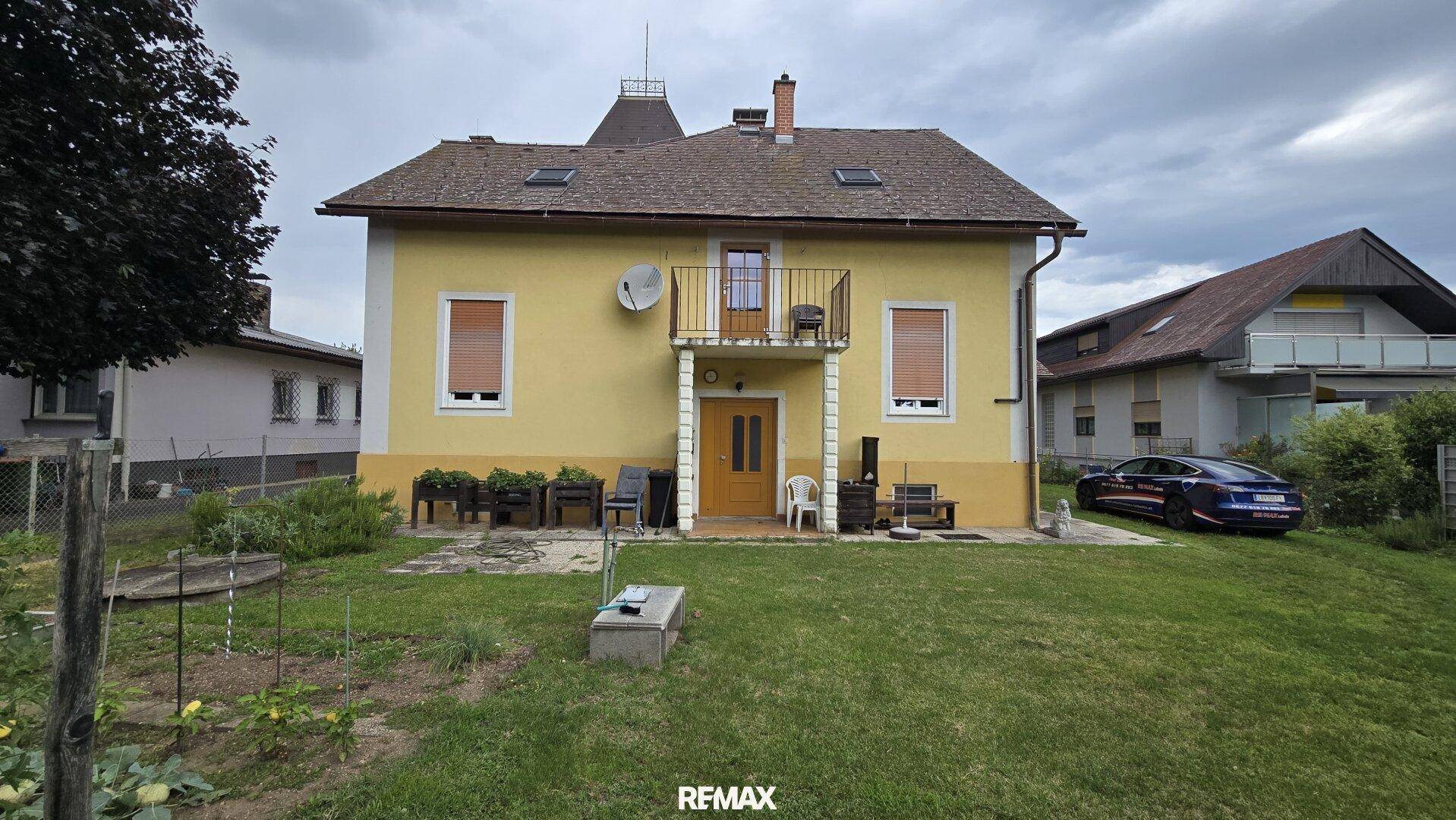 Rückansicht des gelben Hauses mit kleinem Balkon und weitläufigem Gartenbereich.