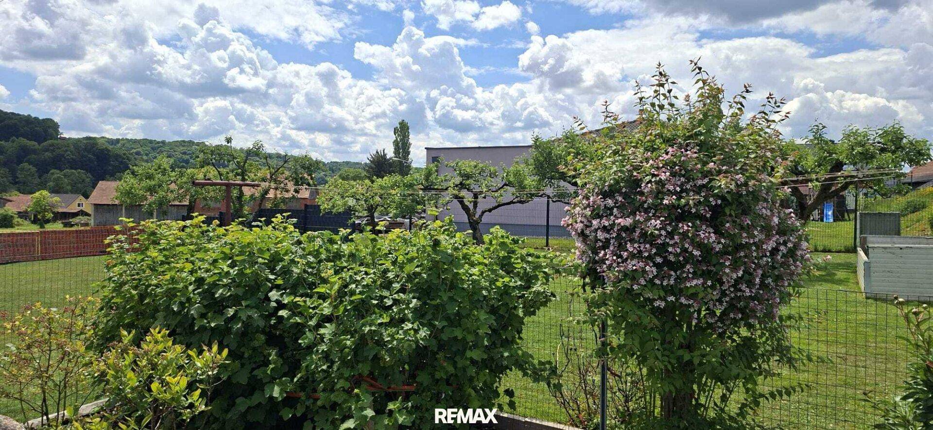 Grüner Garten mit blühenden Sträuchern und Obstbäumen, umgeben von ländlicher Idylle.