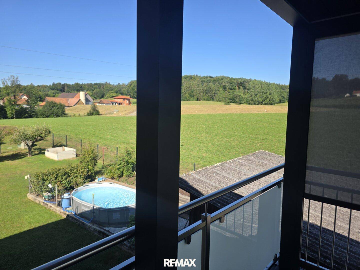 Weitblick vom Balkon über den Garten mit Pool und die grüne Landschaft.