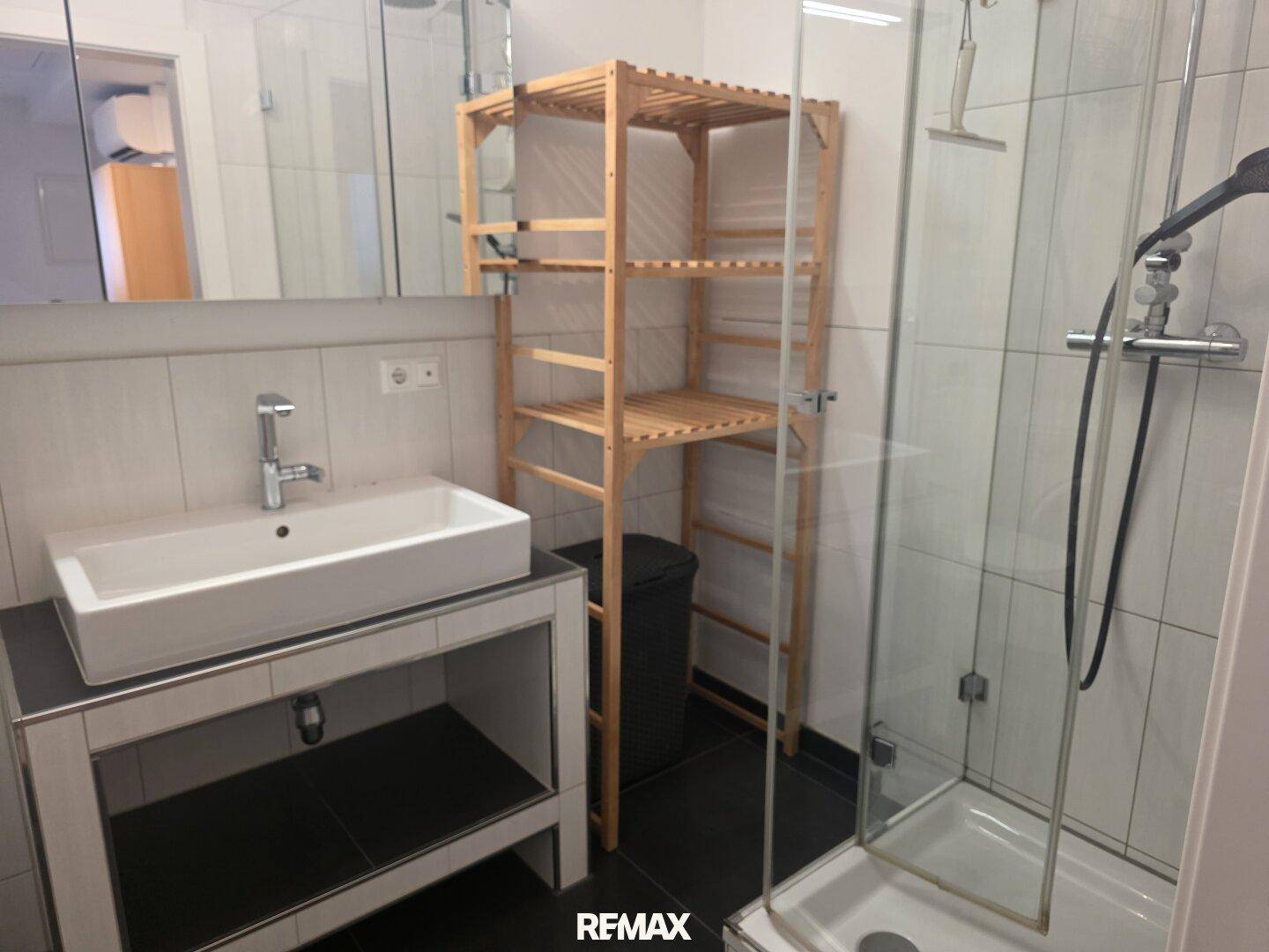 Modernes Badezimmer mit Duschkabine, Aufsatzwaschbecken und Holzregal.