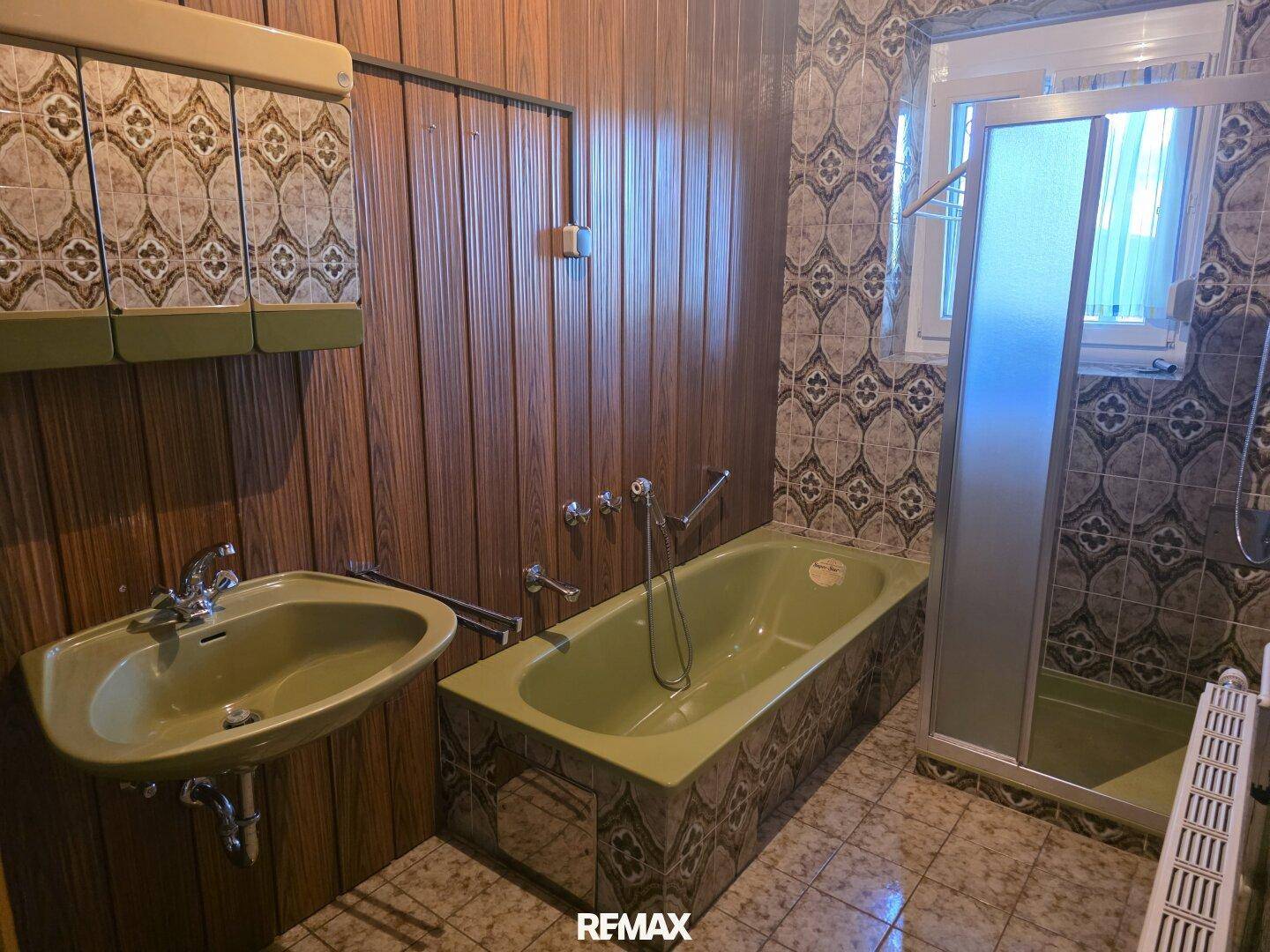 Badezimmer im Stil der 80er Jahre mit grüner Badewanne, Dusche und gemusterten Fliesen.