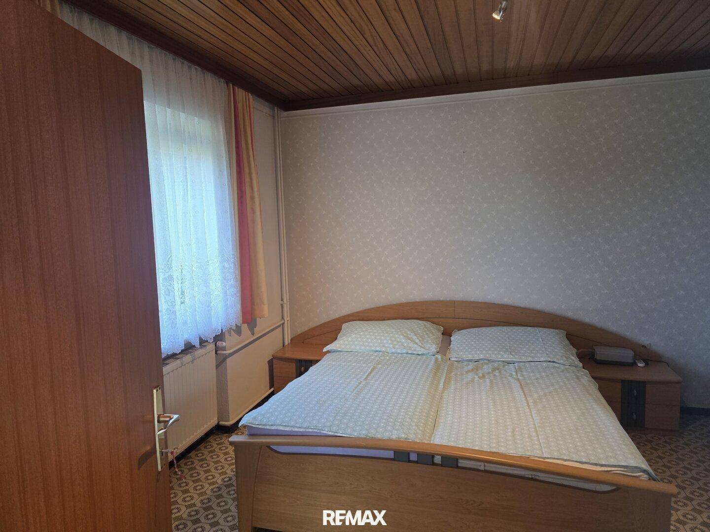 Schlafzimmer mit Holzbett, Holzdecke und gemustertem Teppichboden.