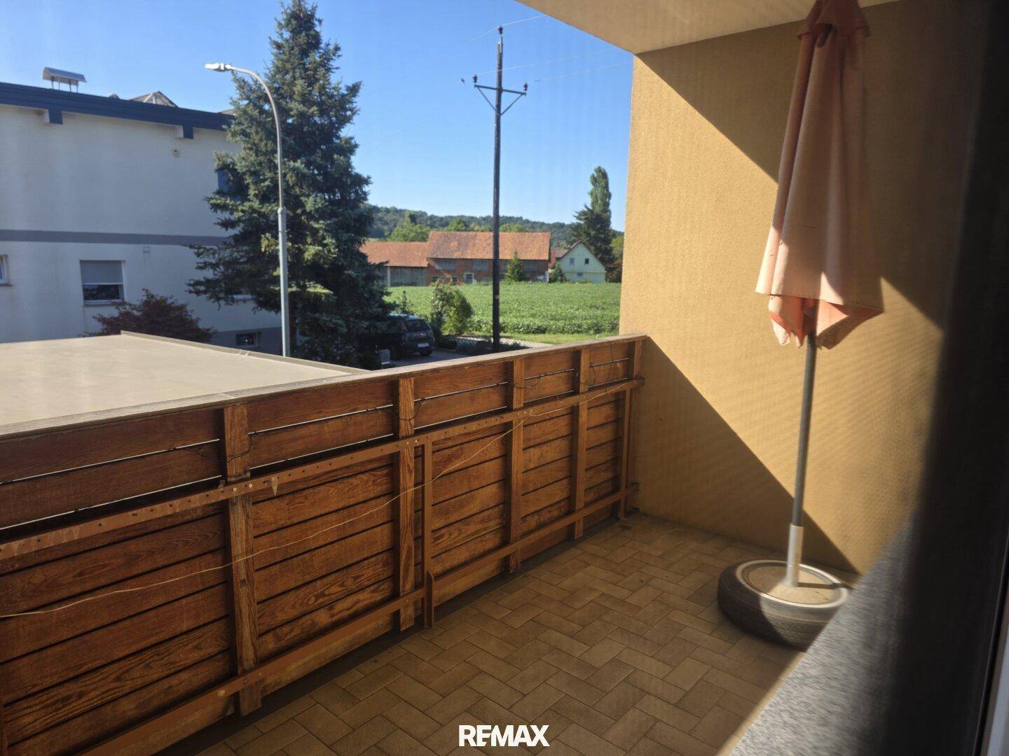 Balkon mit Holzzaun und Blick auf die umliegende Landschaft und Felder.