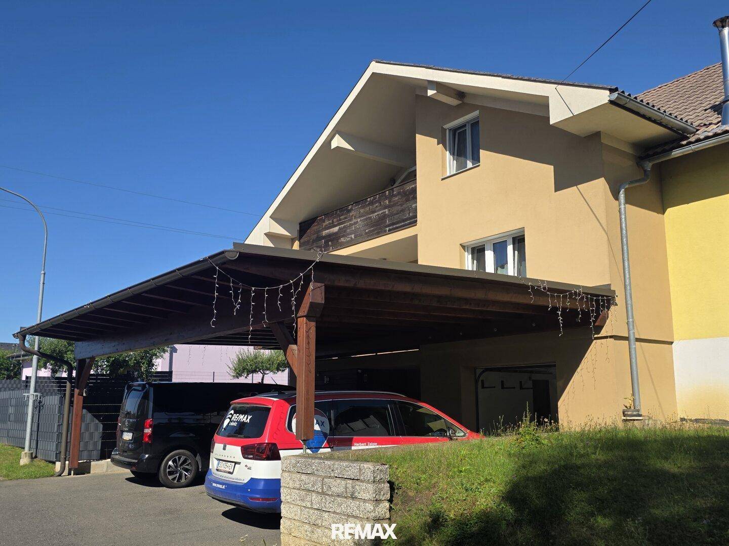 Einfamilienhaus mit Satteldach, überdachtem Carport und gepflegter Außenanlage unter blauem Himmel.