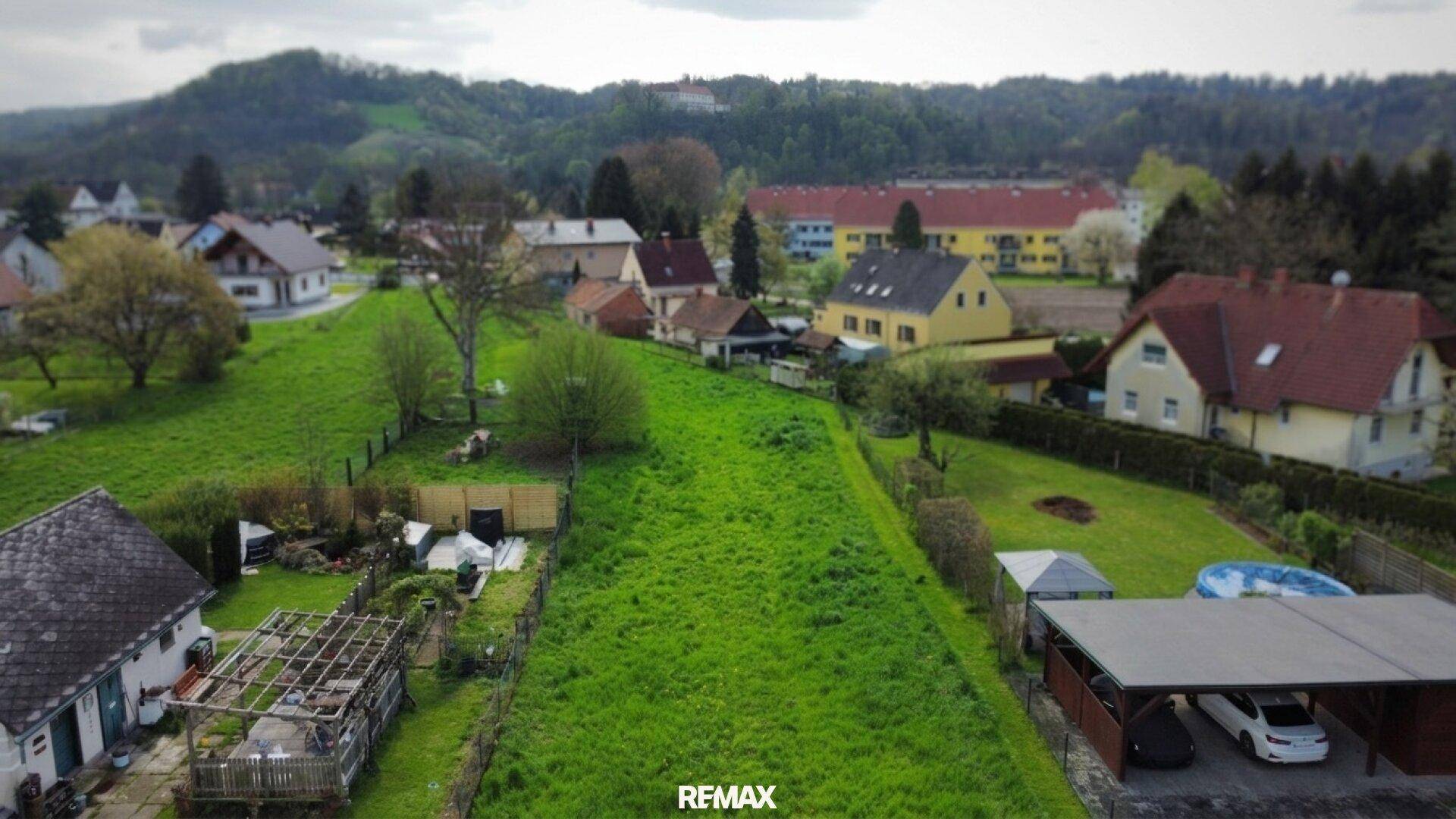 Weitläufiges grünes Grundstück aus der Vogelperspektive mit angrenzenden Wohnhäusern und hügeliger Landschaft.