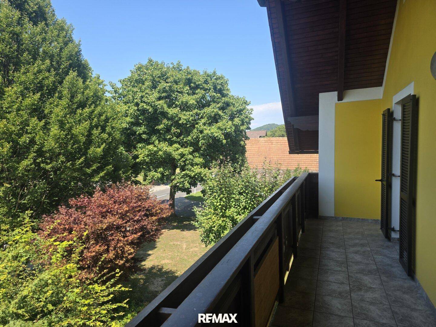 Langer Balkon mit Holzgeländer und Blick auf die grüne Umgebung.