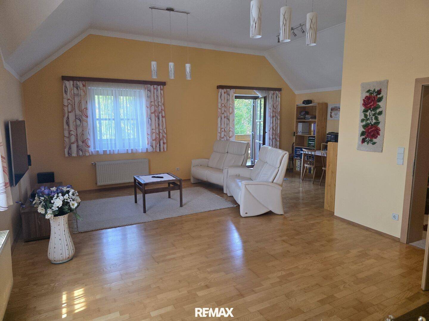 Geräumiges Wohnzimmer mit Holzboden, beigen Sofas und Zugang zu einem Balkon.