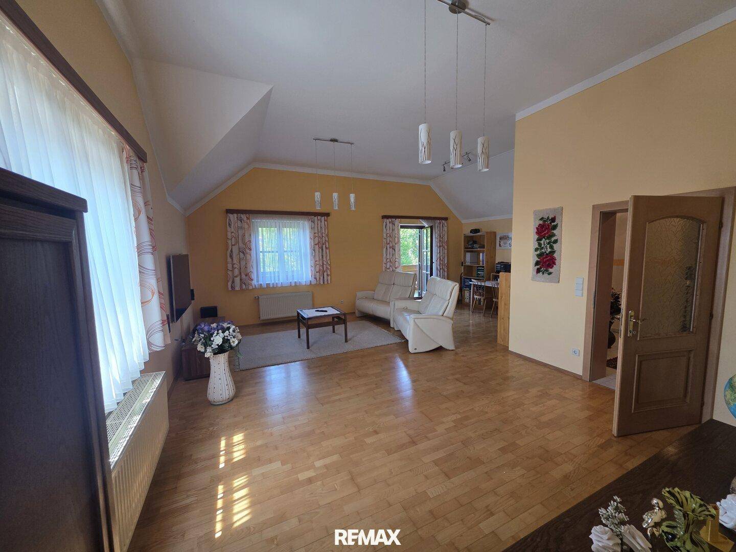 Geräumiges Wohnzimmer mit Holzboden, beigen Sofas und Zugang zu einem Balkon.