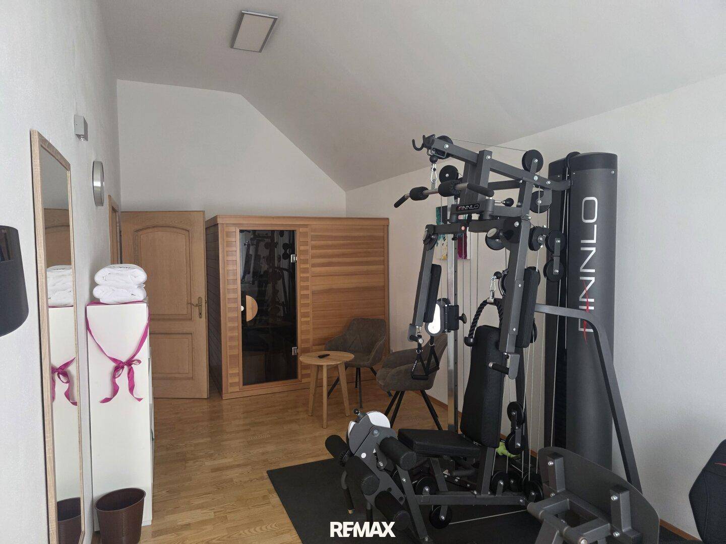 Fitnessraum mit Trainingsgeräten, Spiegeln und einer sichtbaren Sauna.