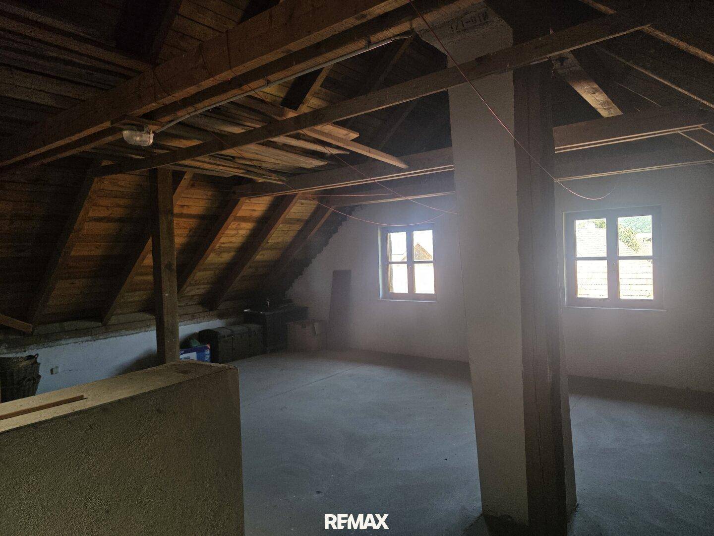 Unausgebauter Dachboden mit sichtbaren Holzbalken und zwei Fenstern.