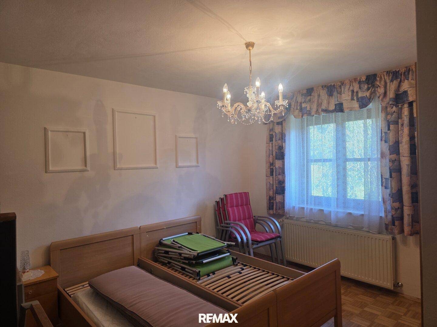 Schlafzimmer mit zwei Einzelbetten, Kronleuchter und Fenster mit Vorhängen.