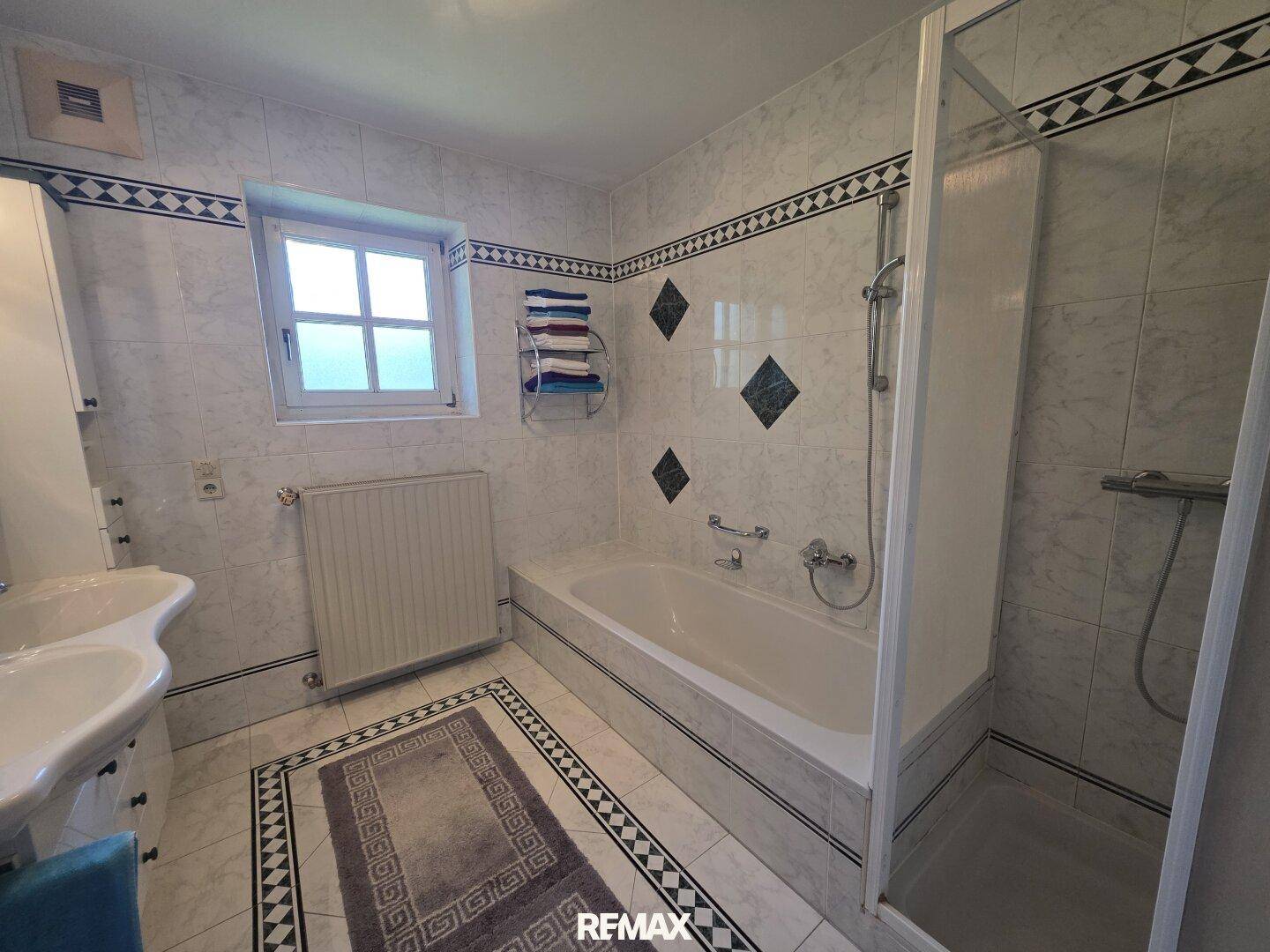 Gefliestes Badezimmer mit Badewanne, Dusche und Fenster in traditionellem Stil.