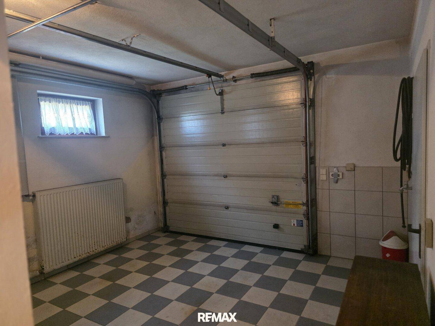 Garage mit kariertem Fliesenboden, Garagentor und einem kleinen Fenster.