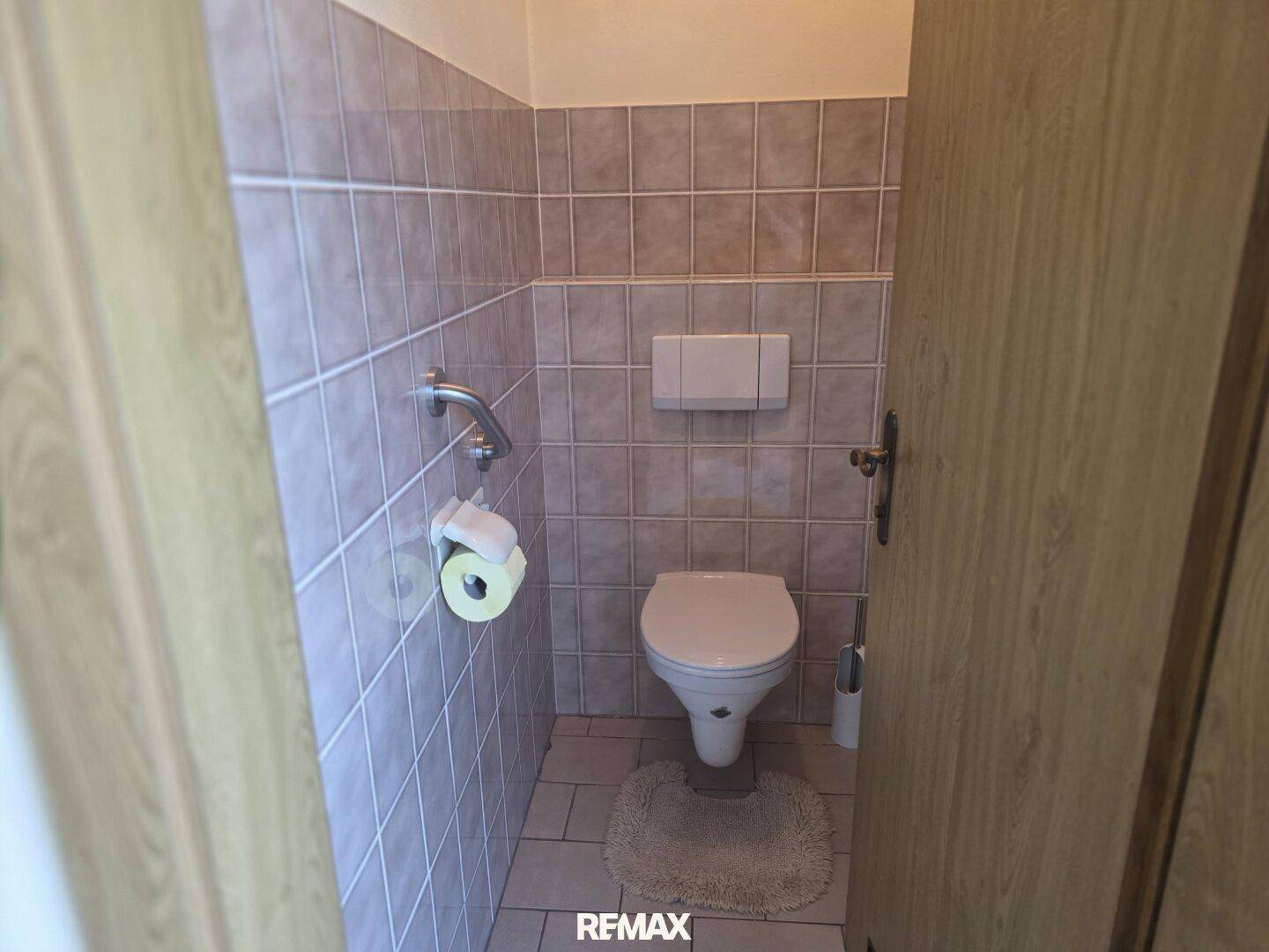 Kleines WC im Keller mit Fliesen, Wand-WC und Haltegriff.