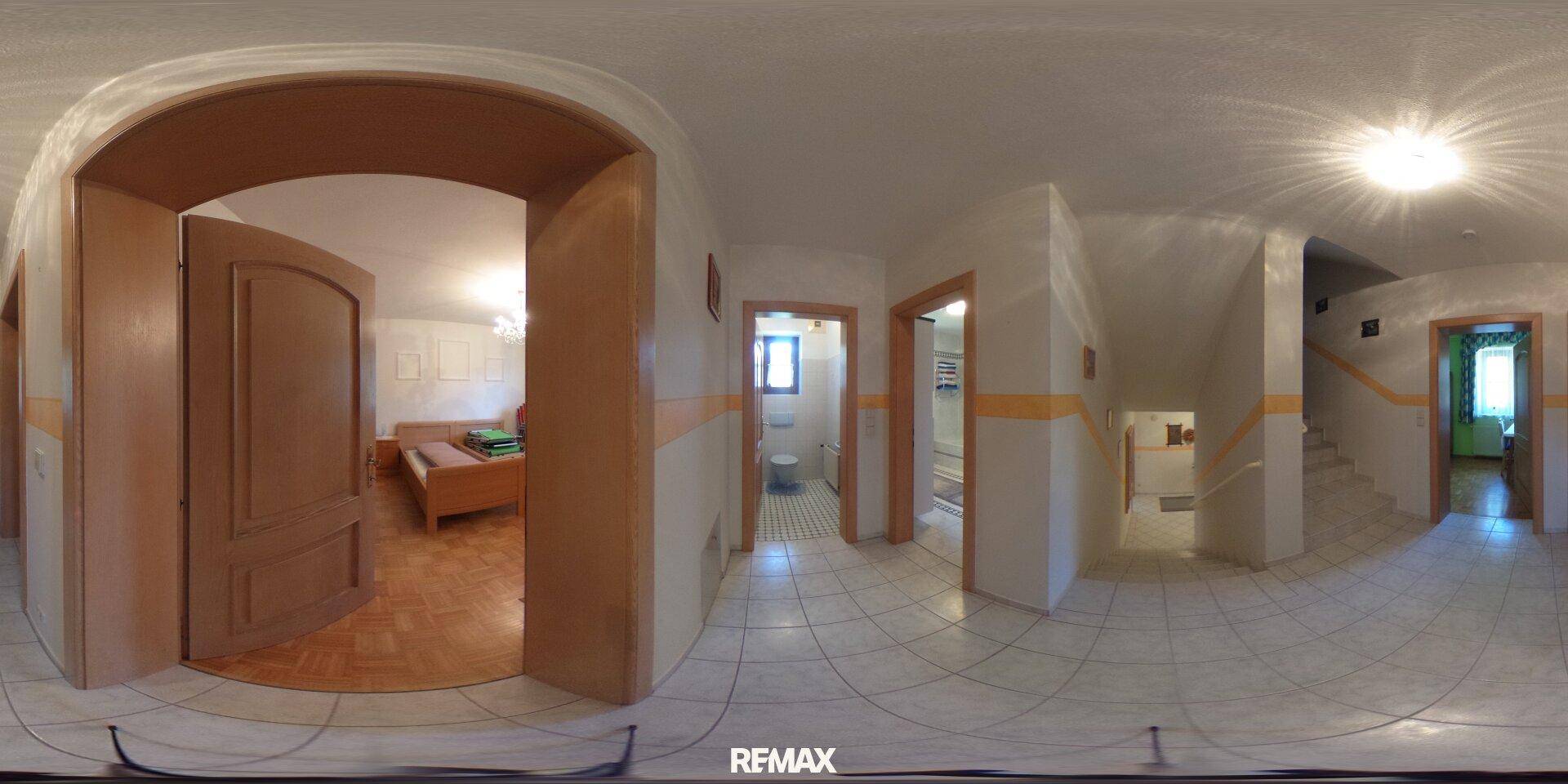 Heller Flur mit Fliesenboden, Holztüren und Zugang zu einem Schlafzimmer sowie einer Treppe.