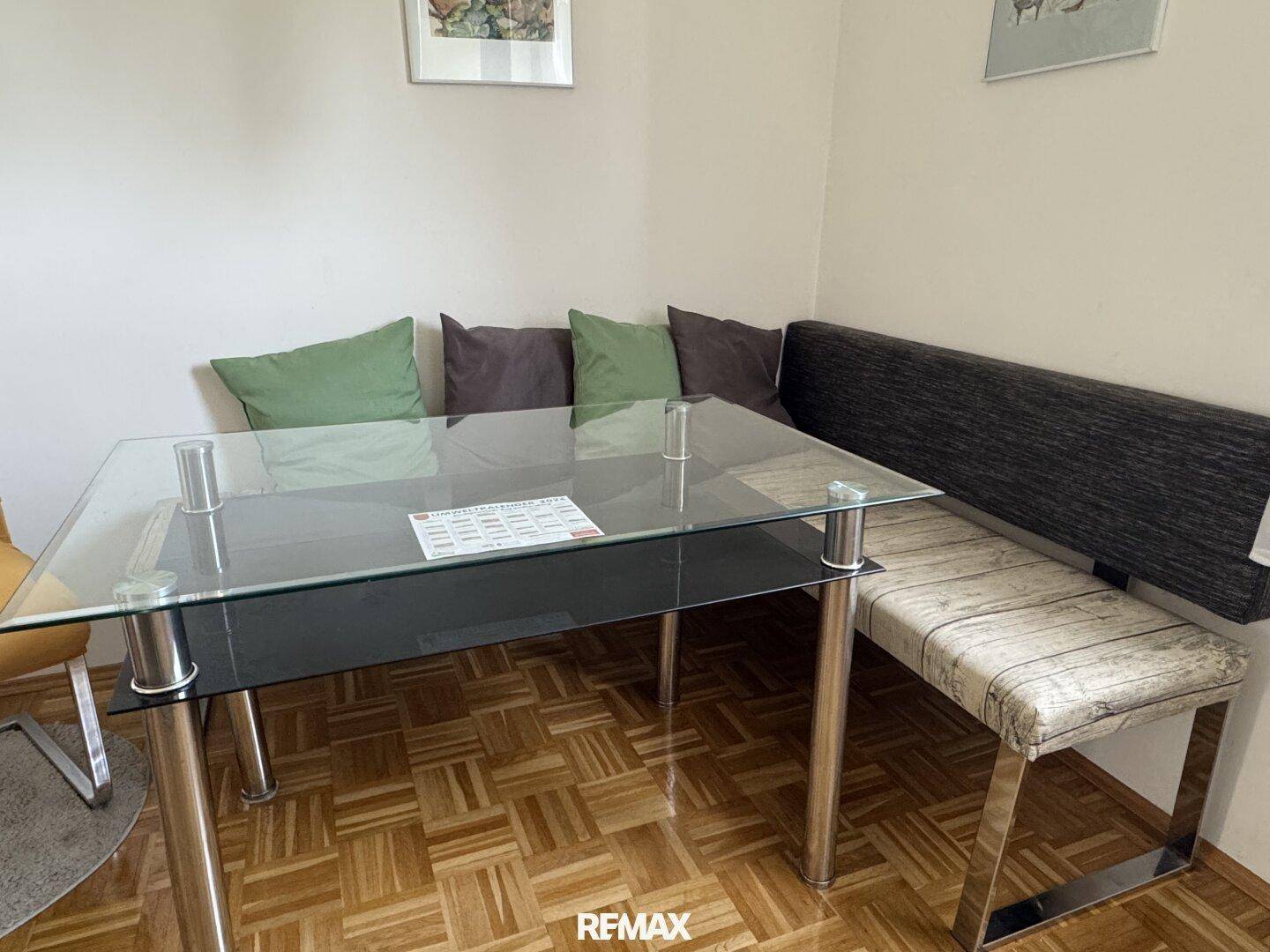 Essbereich in der Küche mit modernem Glastisch und bequemer Eckbank auf Parkettboden.