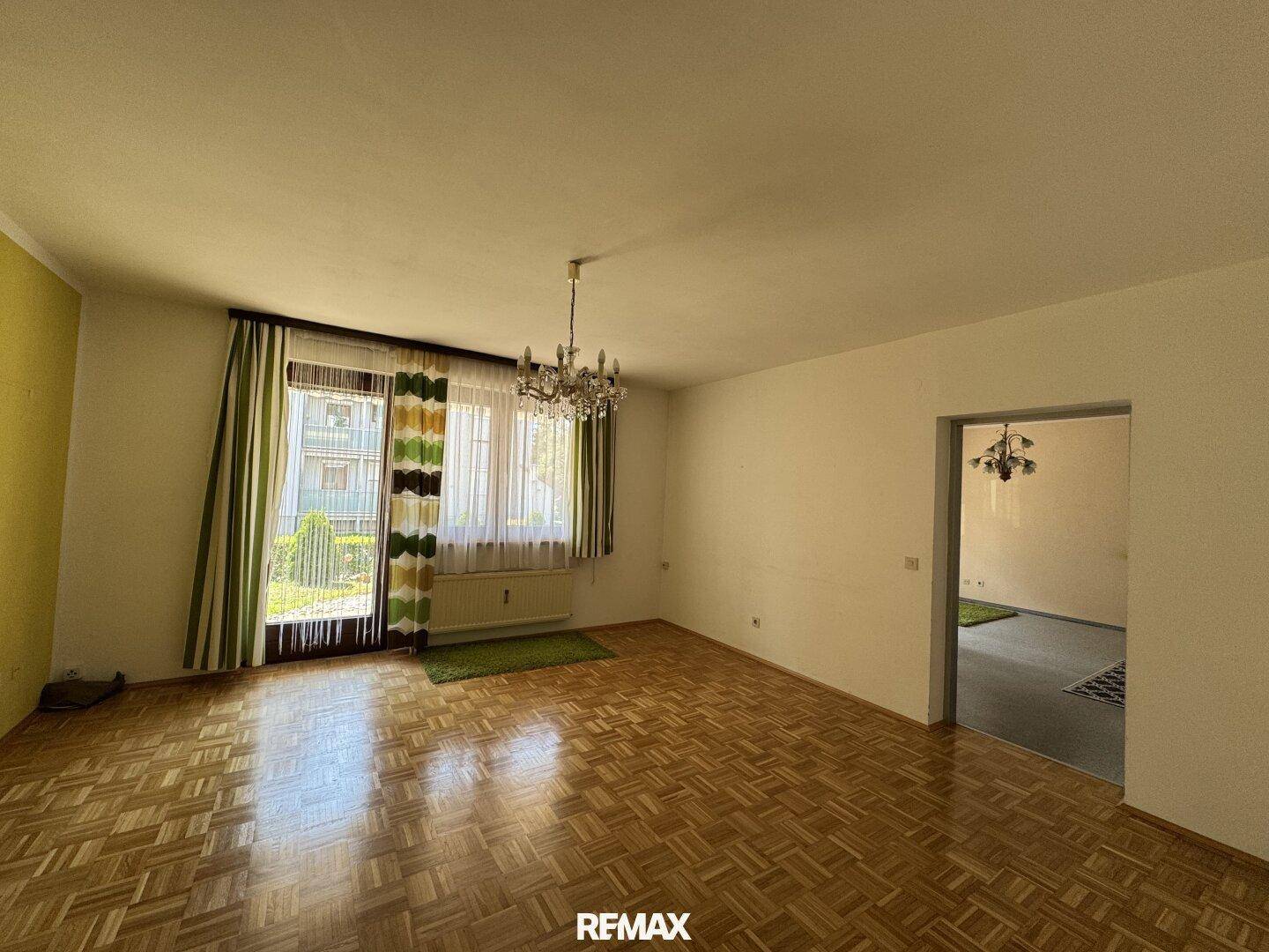Geräumiges Wohnzimmer mit Parkettboden, klassischem Kronleuchter und Zugang zum Außenbereich.