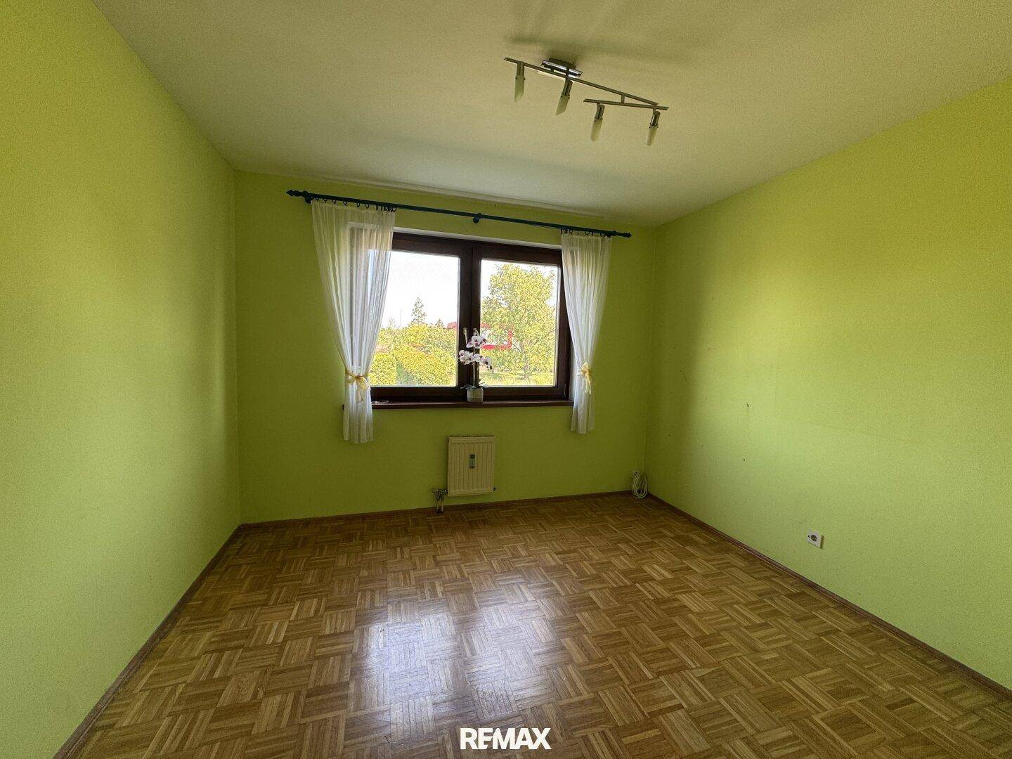 Helles Schlafzimmer mit grünen Wänden, Parkettboden und einem Fenster mit Blick ins Grüne.