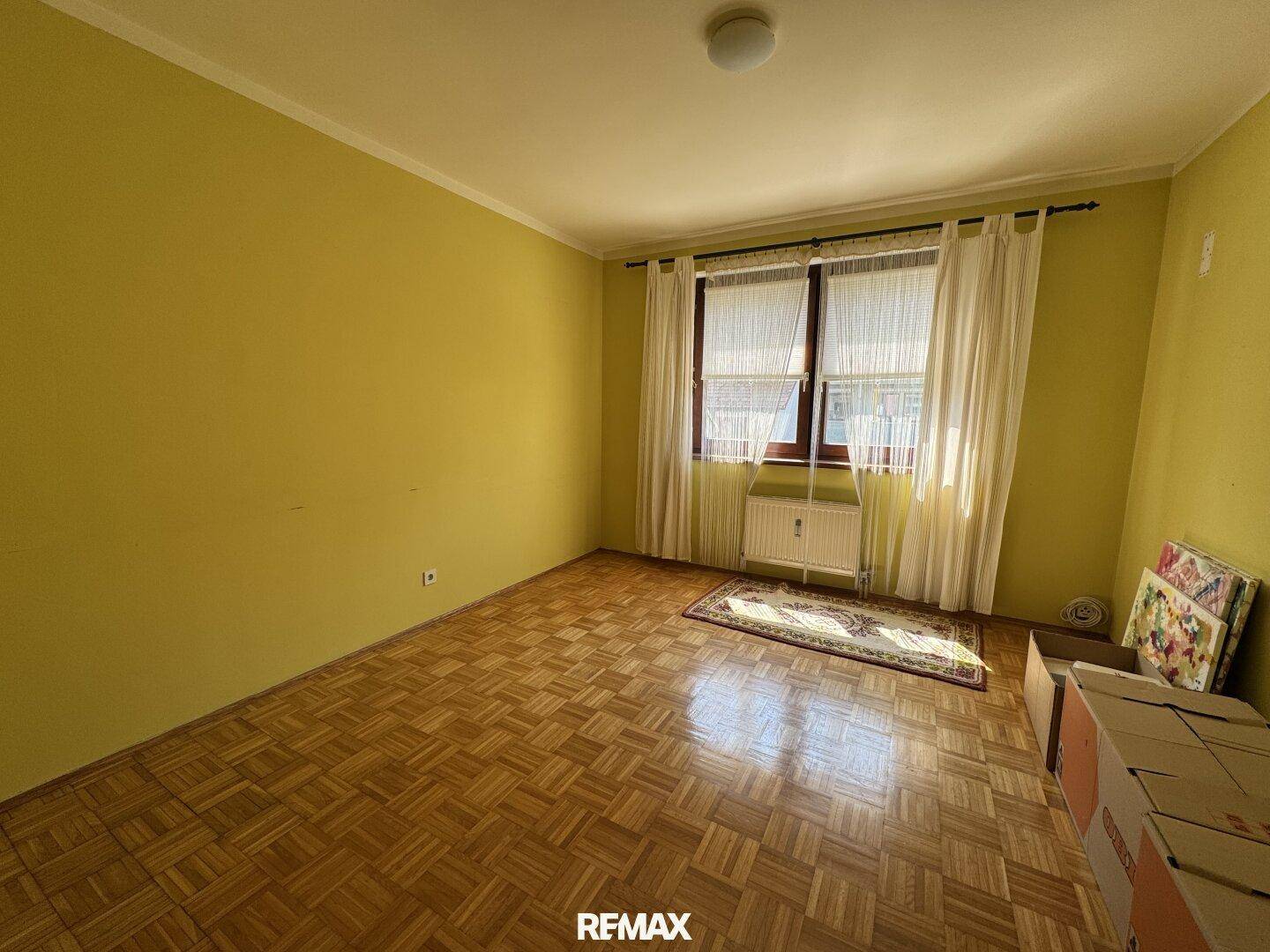 Geräumiges Schlafzimmer mit gelben Wänden, Parkettboden und einem großen Fenster für viel Licht.
