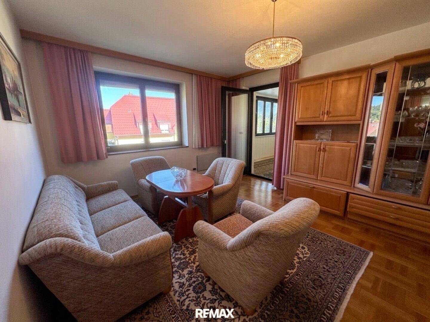 Gemütliches Wohnzimmer mit beigen Polstermöbeln, Parkettboden und Zugang zum Balkon.
