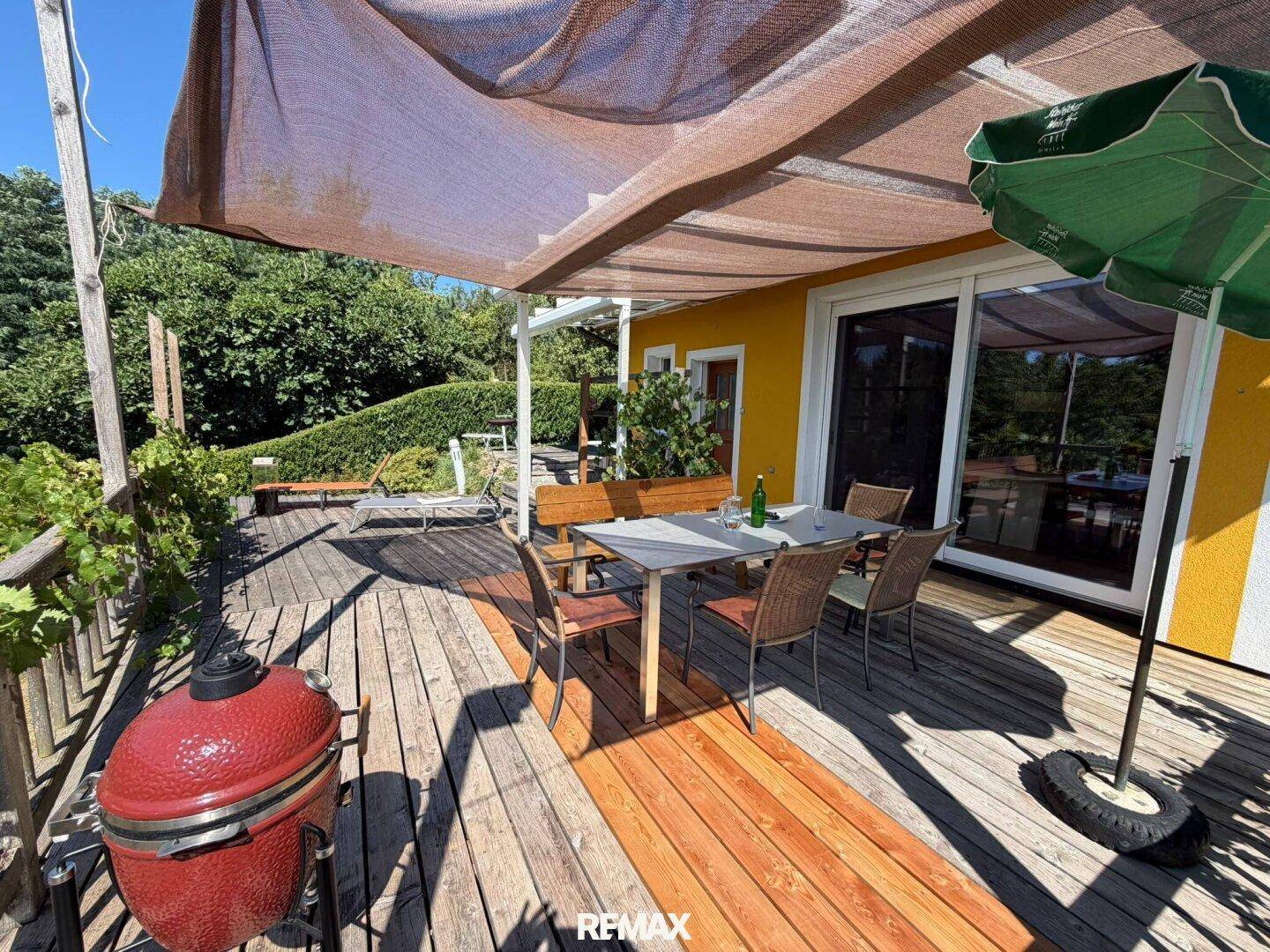 Gemütliche Terrasse mit Esstisch, großem Grill und Sonnenschutz, ideal für Mahlzeiten im Freien.
