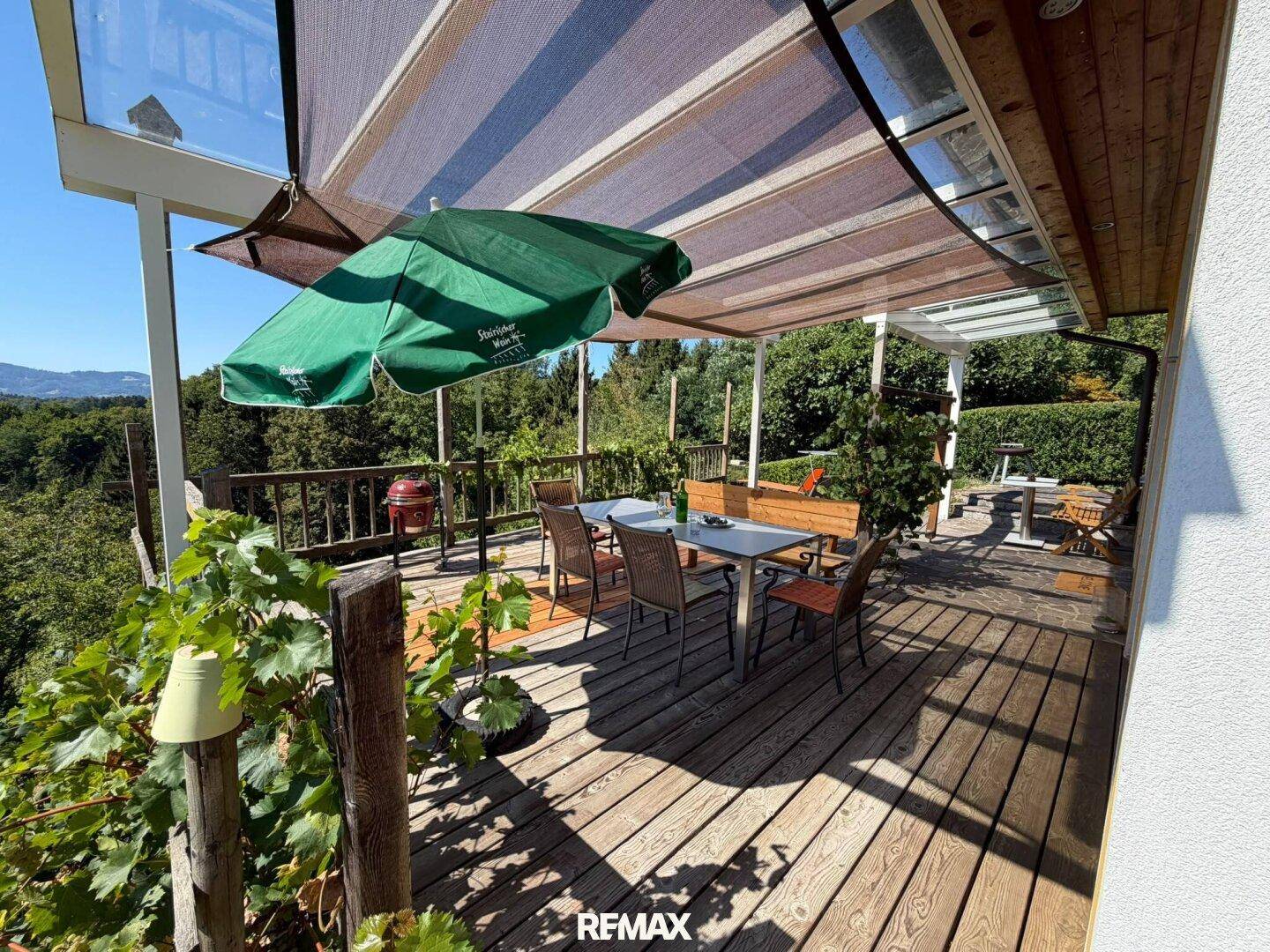 Geräumige Terrasse mit Essbereich und Sonnenschutz, umgeben von üppigem Grün und Natur.