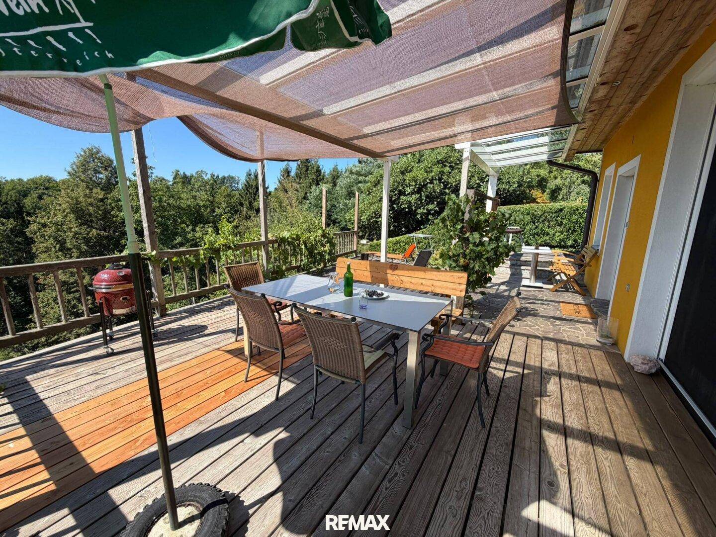 Große Holzterrasse mit Essbereich und Sonnenschirm, bietet viel Platz zum Entspannen im Freien.