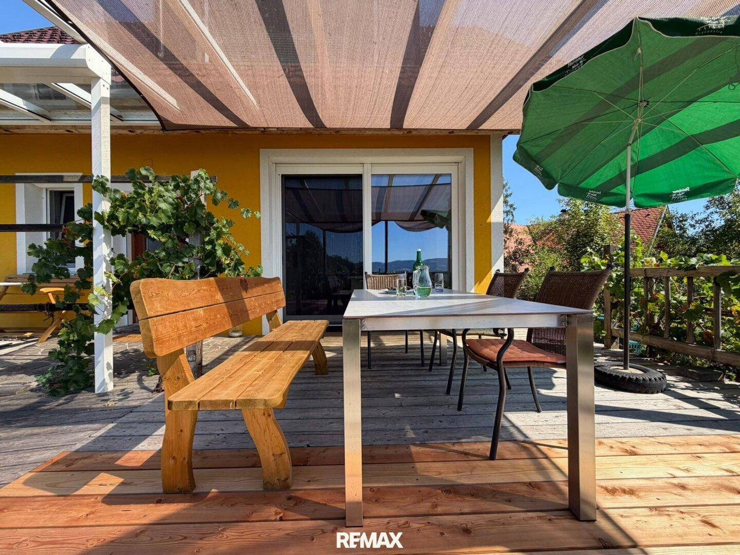 Terrasse mit Holzsitzbank und Esstisch unter Sonnenschutz, ideal für gesellige Stunden.