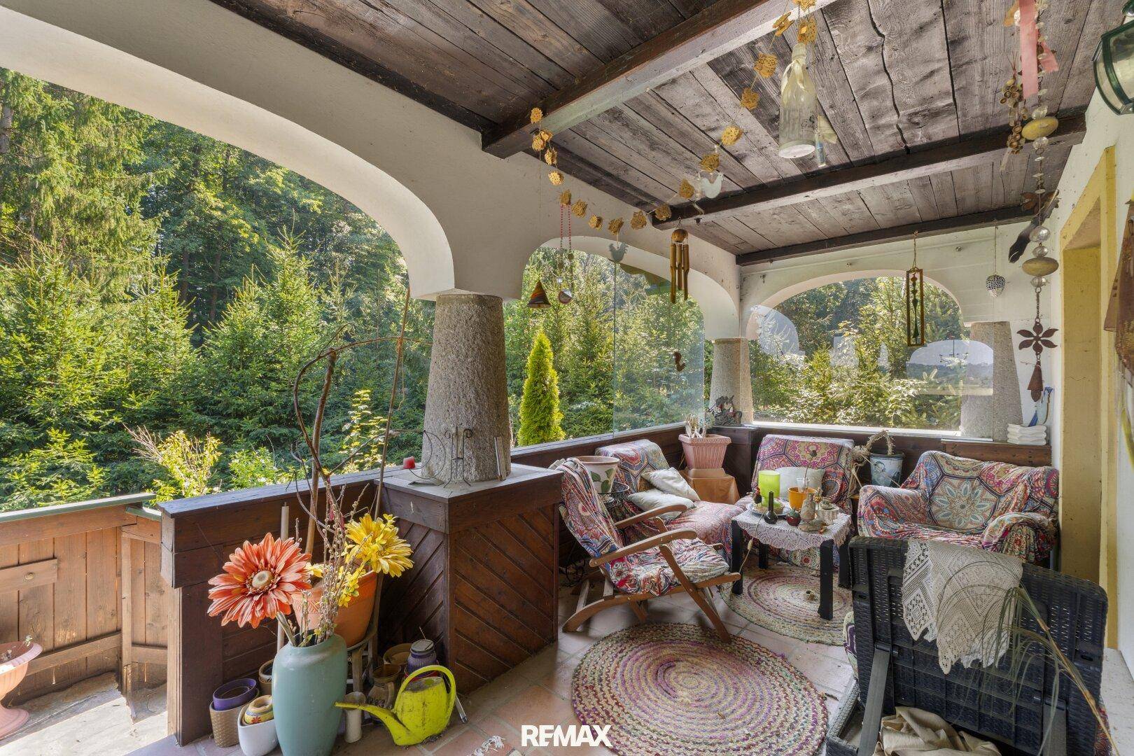 Gemütliche Loggia mit Sitzgelegenheiten, Holzbalkendecke und Blick auf den umliegenden Wald.