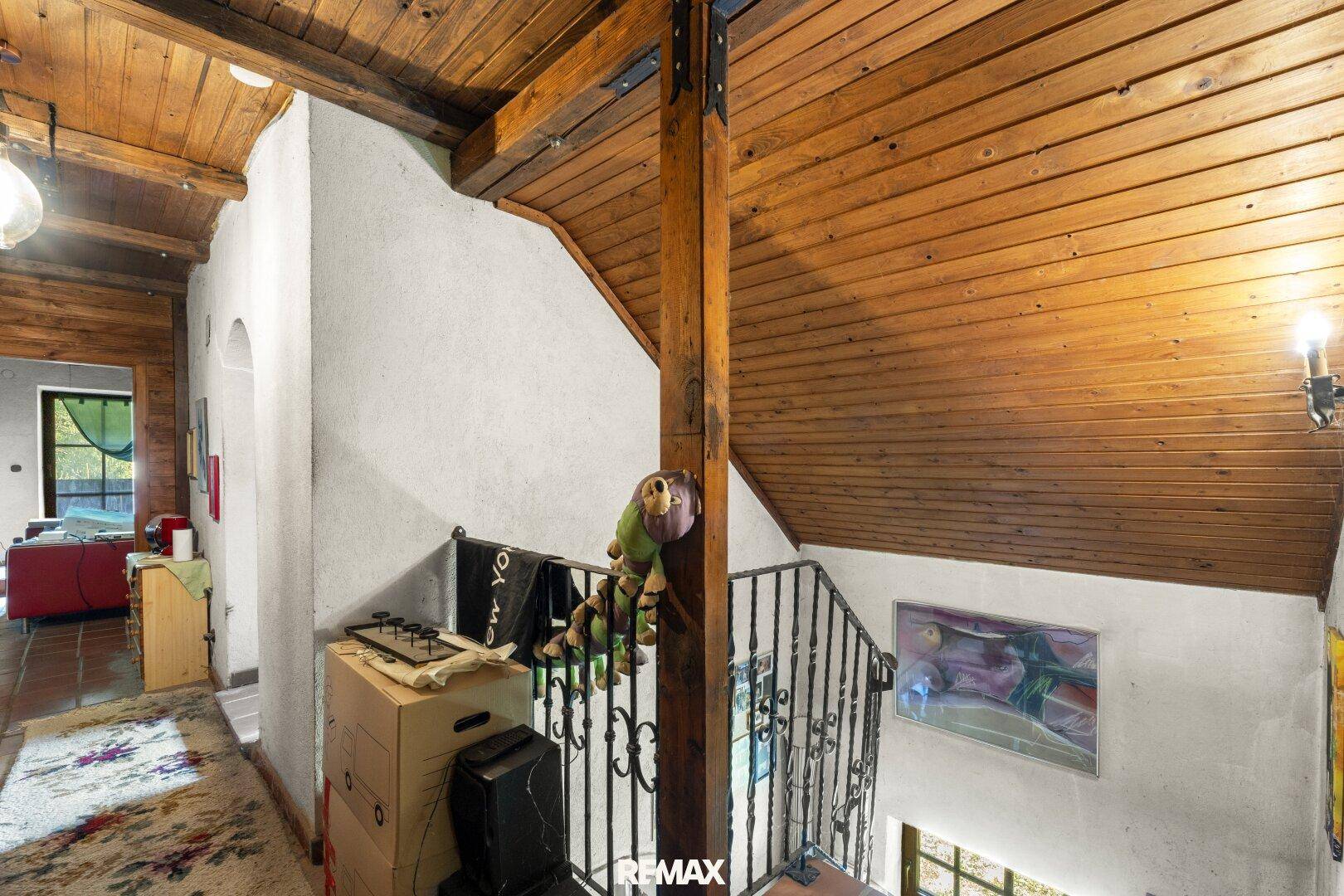 Treppenaufgang mit schmiedeeisernem Geländer, Holzbalken und Holzverkleidung an der Decke.