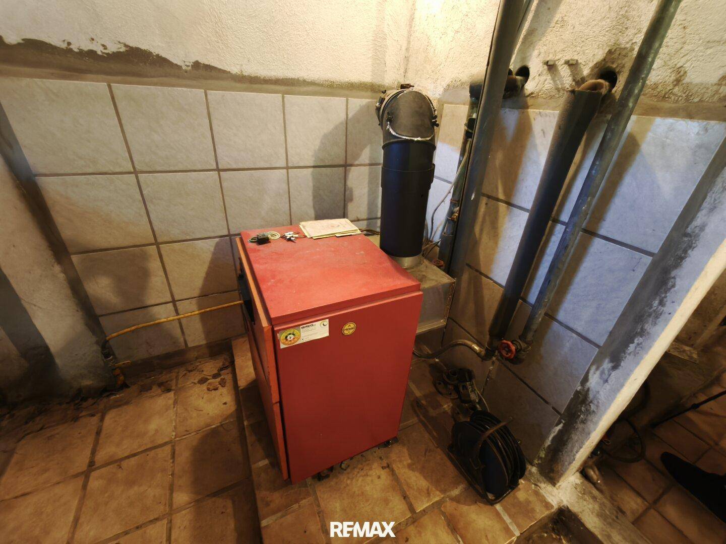 Heizraum mit einem roten Heizkessel und sichtbaren Rohrleitungen, ausgestattet mit Fliesenboden.