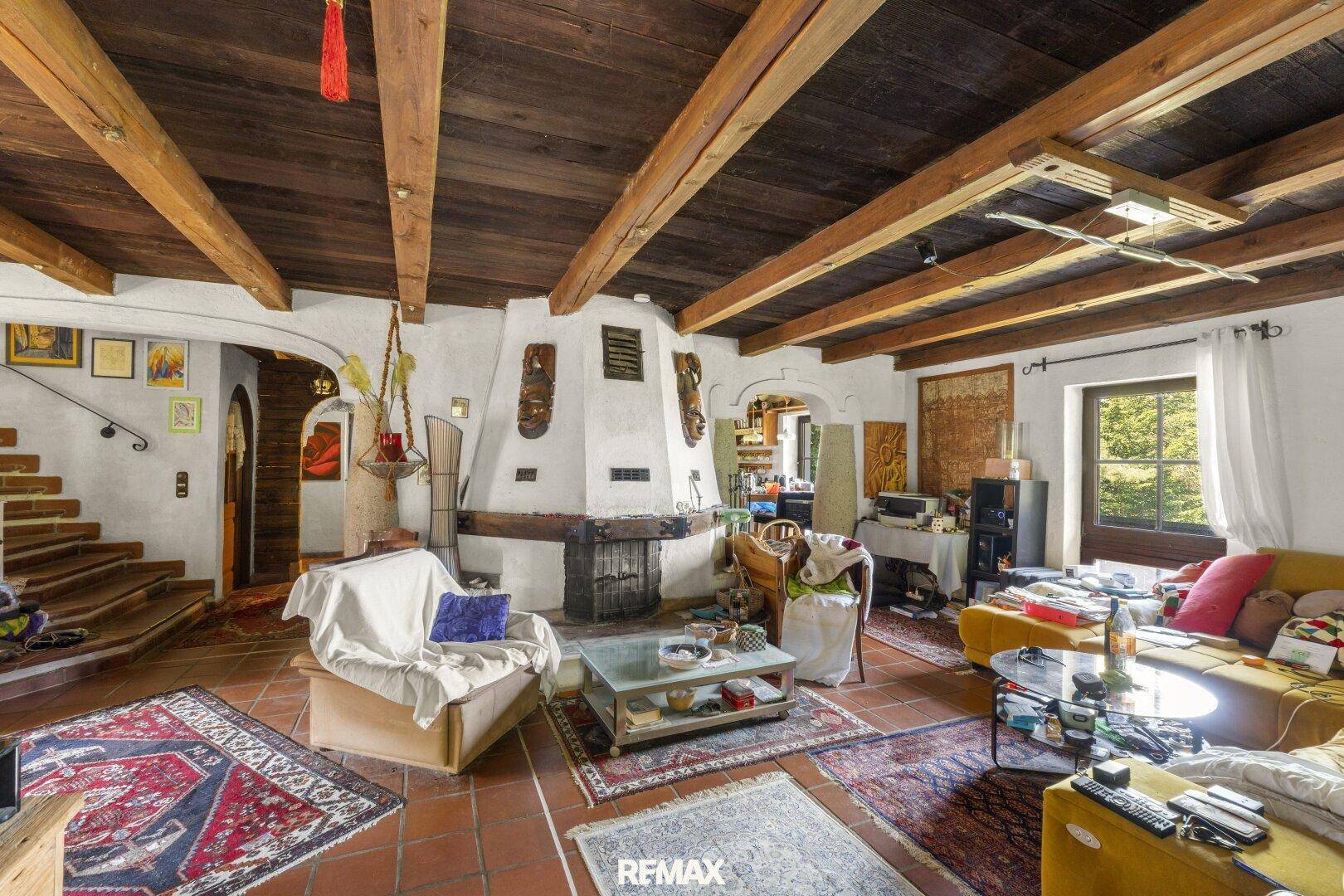 Rustikales Wohnzimmer mit großem Kamin, Holzbalkendecke und Terrakottaboden, gemütlich eingerichtet.