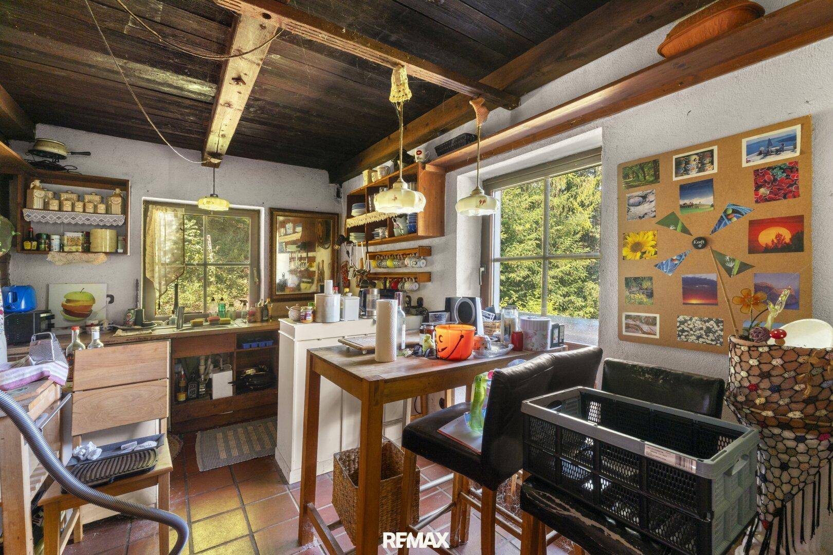 Rustikale Küche mit Holzbalkendecke, Terrakottaboden und einem Esstisch mit Blick ins Grüne.
