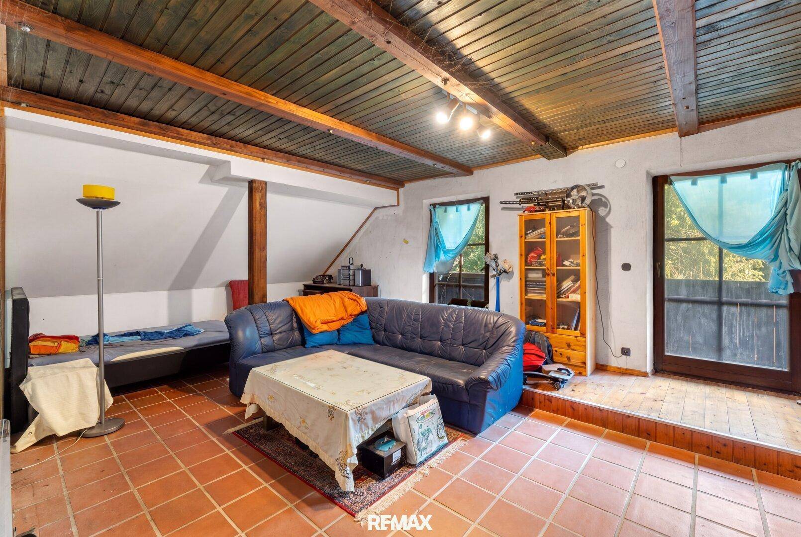 Geräumiges Dachgeschosszimmer mit Holzbalkendecke, Terrakottaboden und Zugang zu einem Außenbereich.