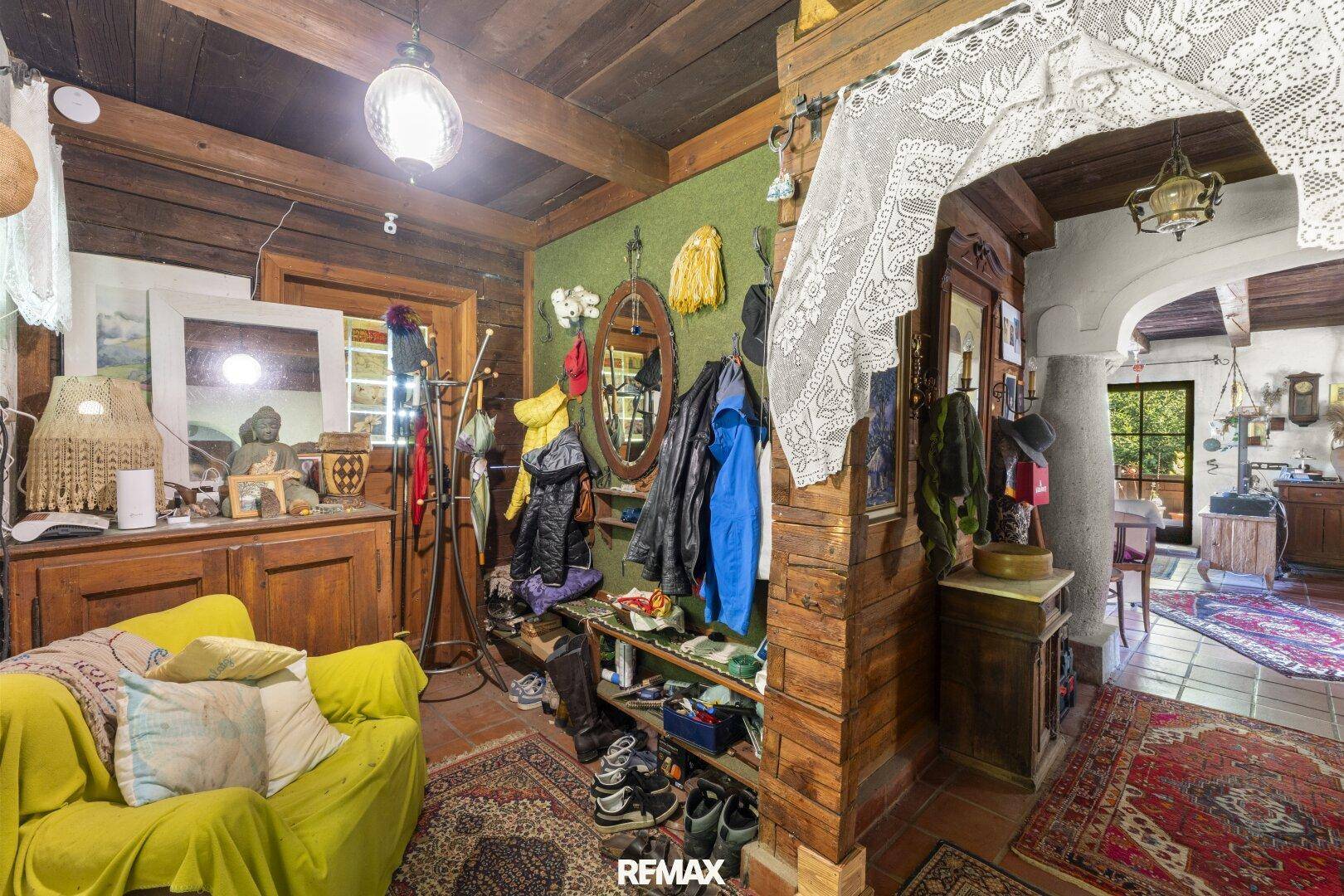 Rustikaler Eingangsbereich mit Holzbalkendecke, grüner Wand und vielen persönlichen Gegenständen.